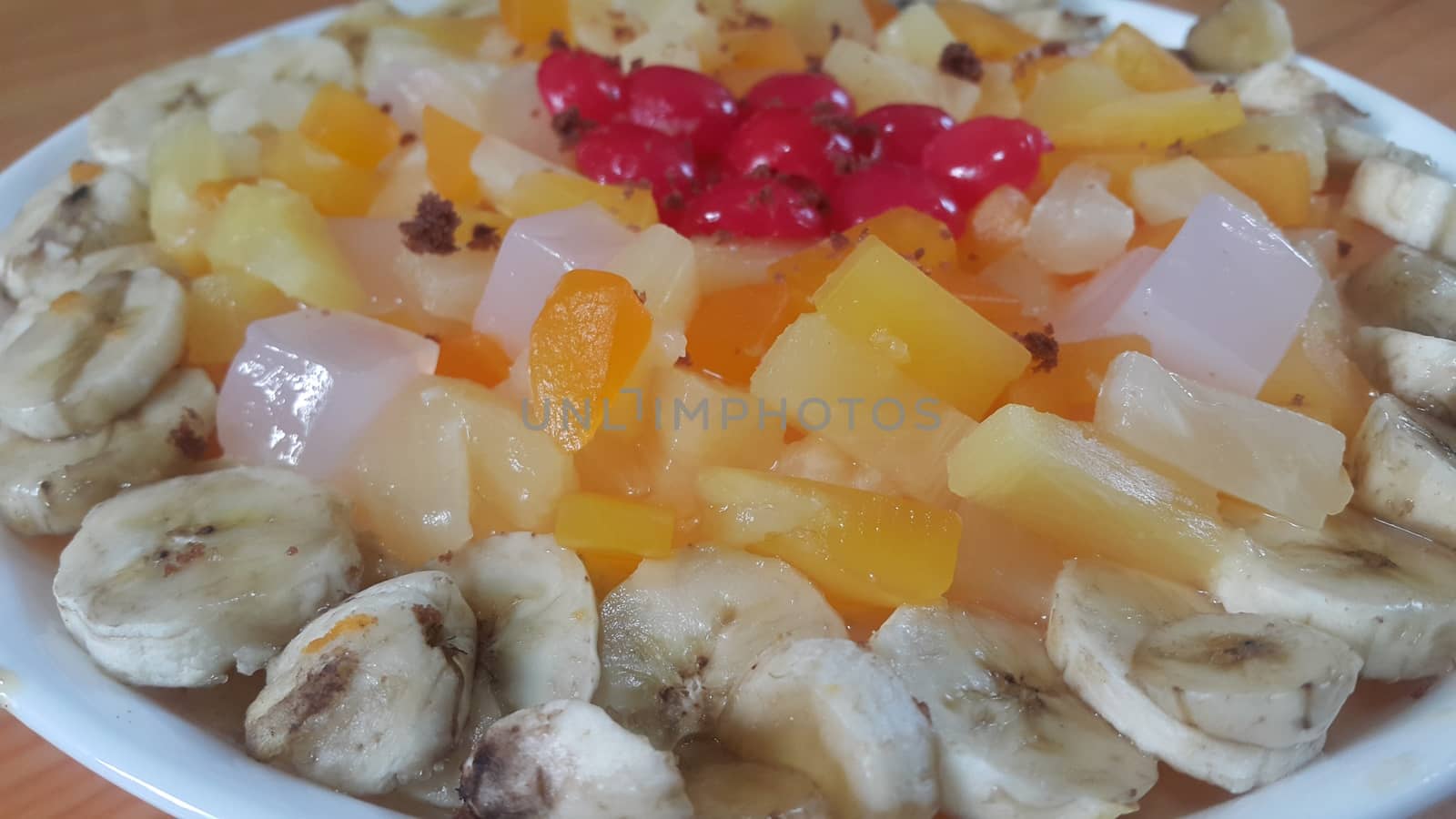 Creamy tasty sweet fruit trifle over custard with banana slices layered on surface on wooden floor. A top view of home made fruit trifle, a products for dessert after meal.
