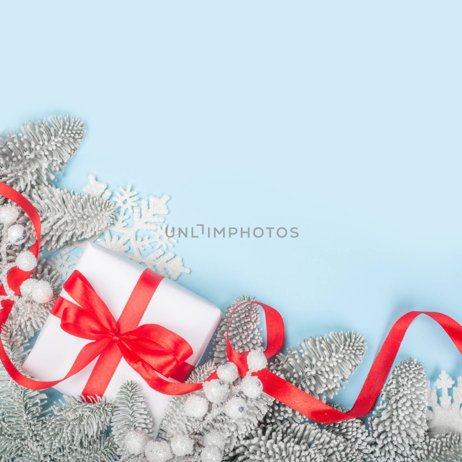Frosted fir tree twigs and Christmas decorative gift with red ribbon on blue background with copy space for text template flat lay top view design