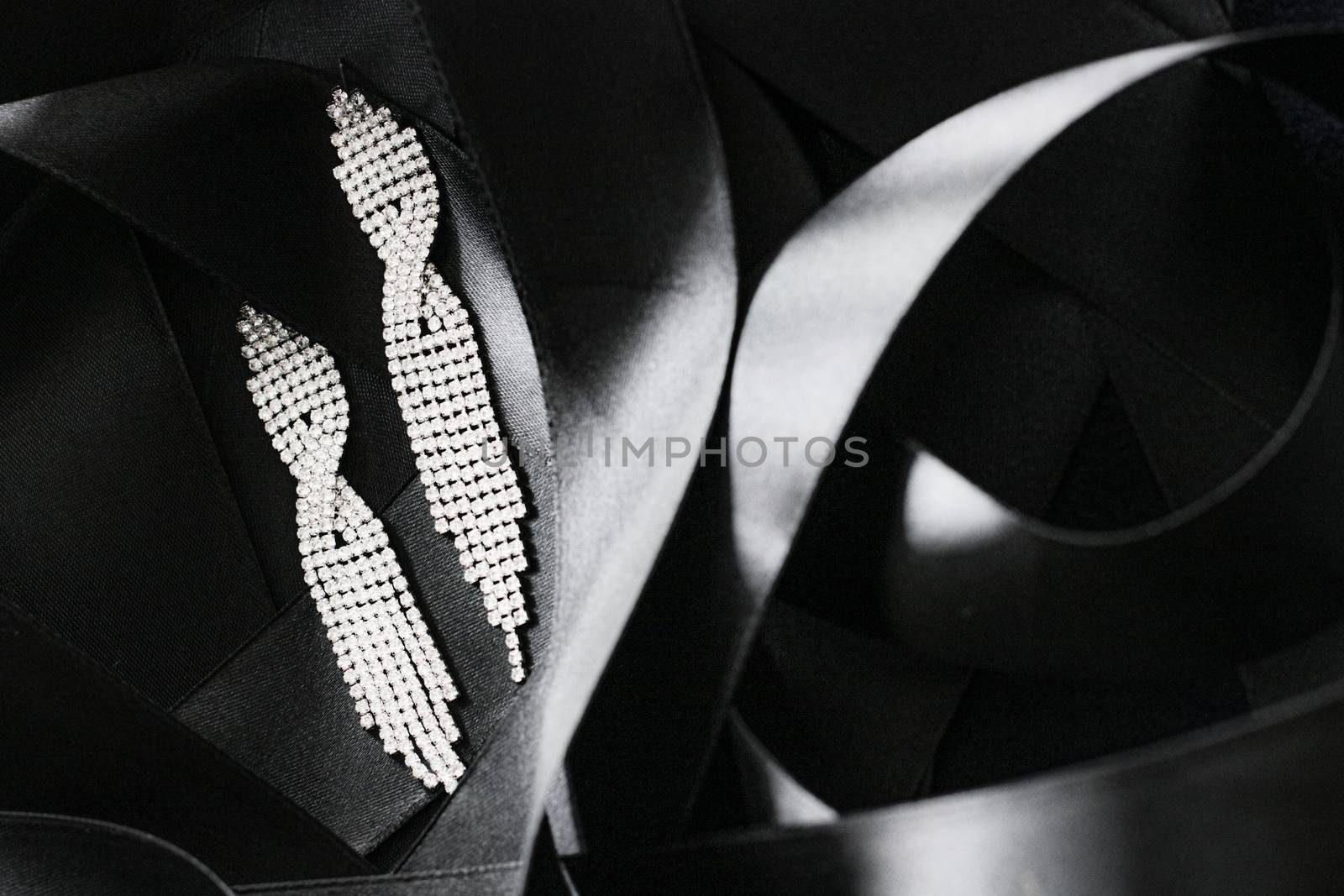 Luxury diamond earrings on black silk ribbon as background, jewelry and fashion brand by Anneleven