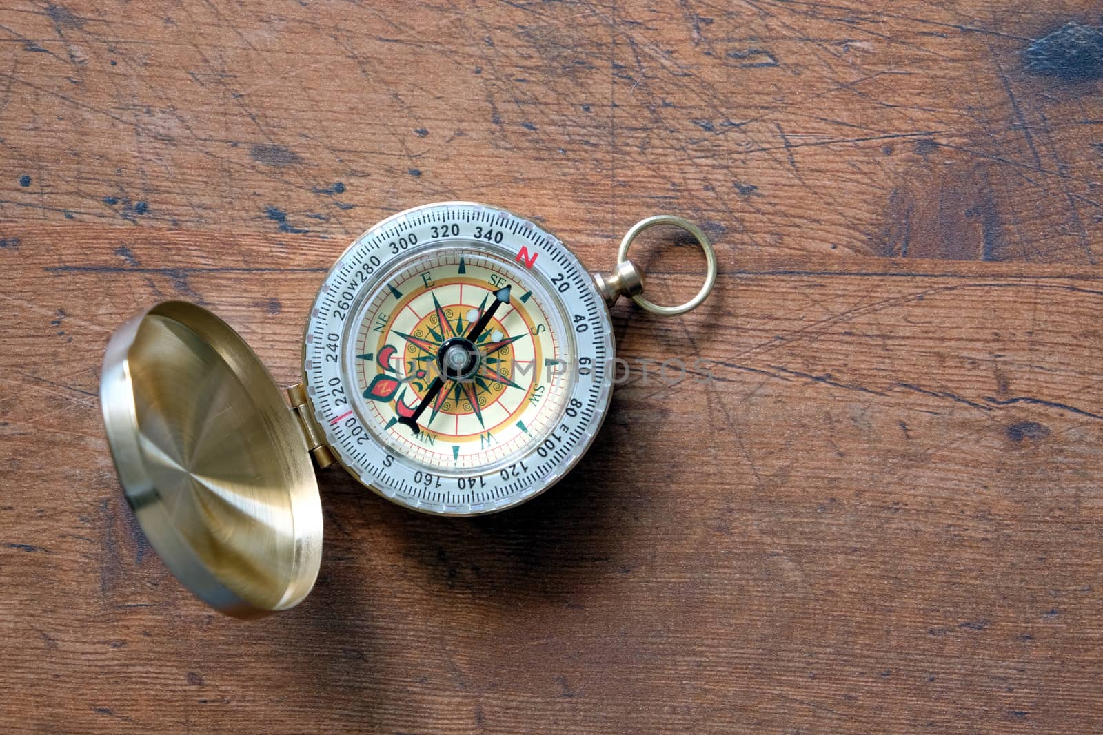 Old compass in opened brass case on vintage brown wooden background shown to North direction top view closeup by dymaxfoto