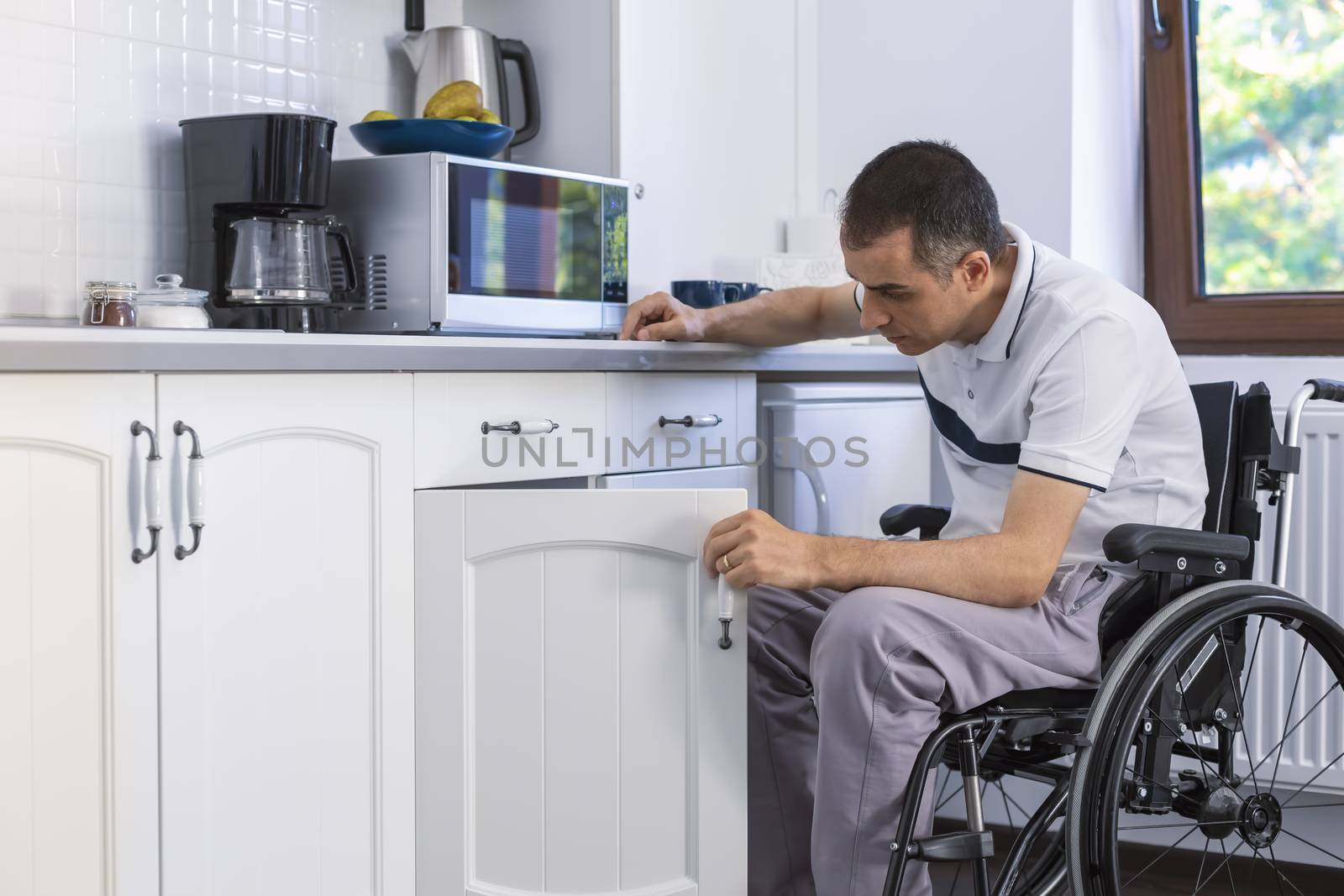 Young Handicapped Man Sitting On Wheelchair In Kitchen. Focus on his face.