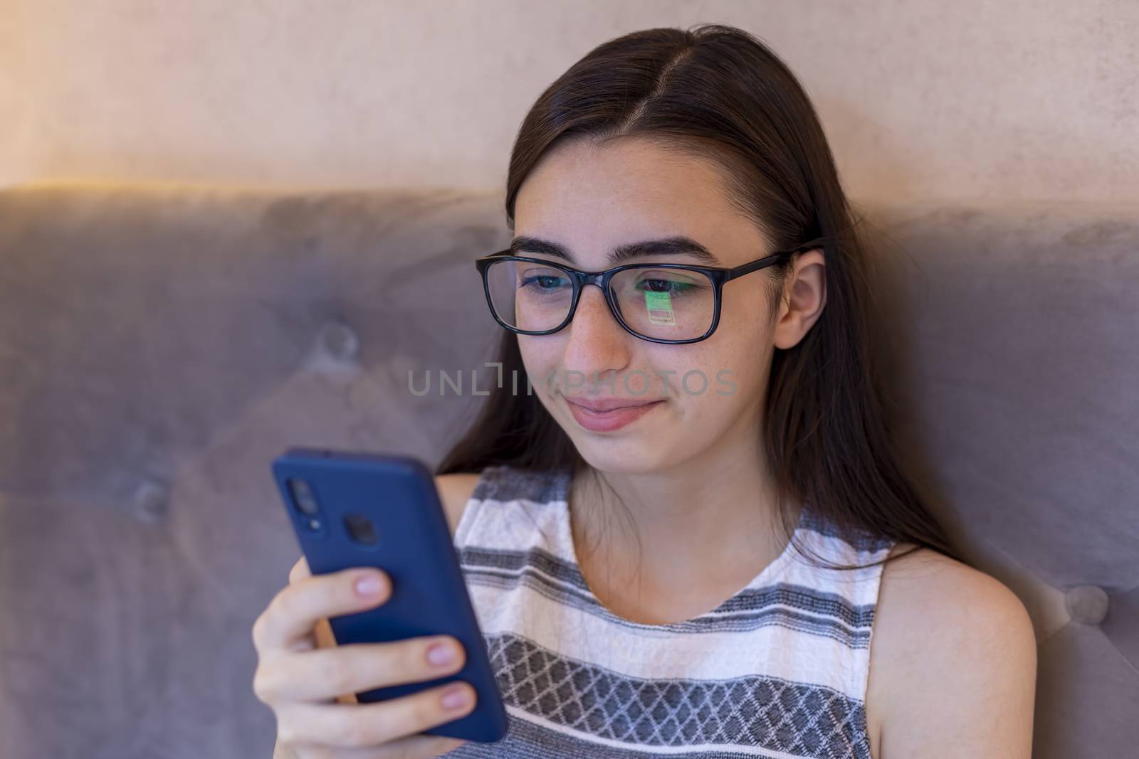Young Caucasian girl with glasses sit rest on sofa and browsing internet on cellphone, millennial female in spectacles texting messaging on smartphone, read news or shopping online