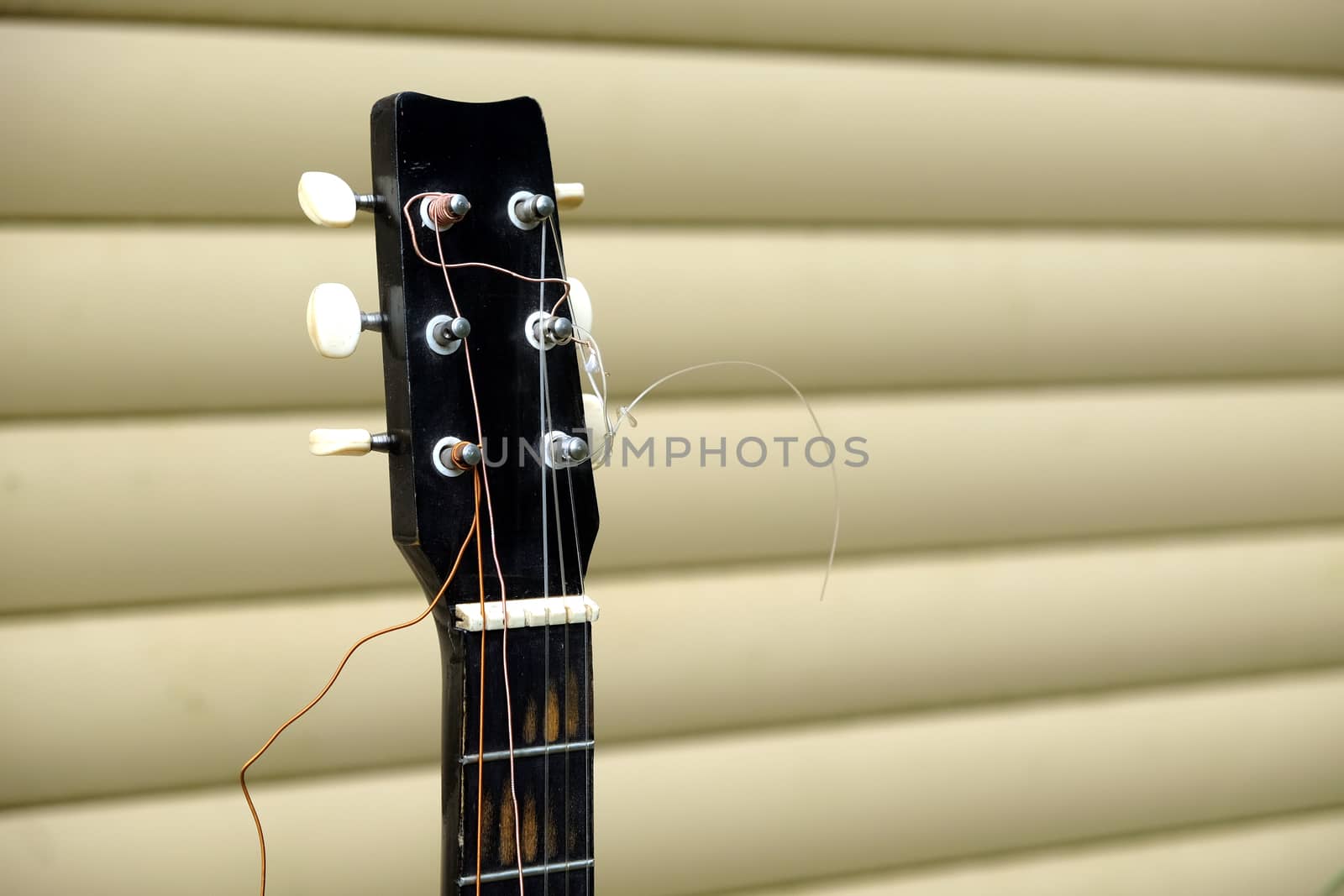 Guitar neck and head in bad condition with broken strings in front of house wall side view closeup by dymaxfoto