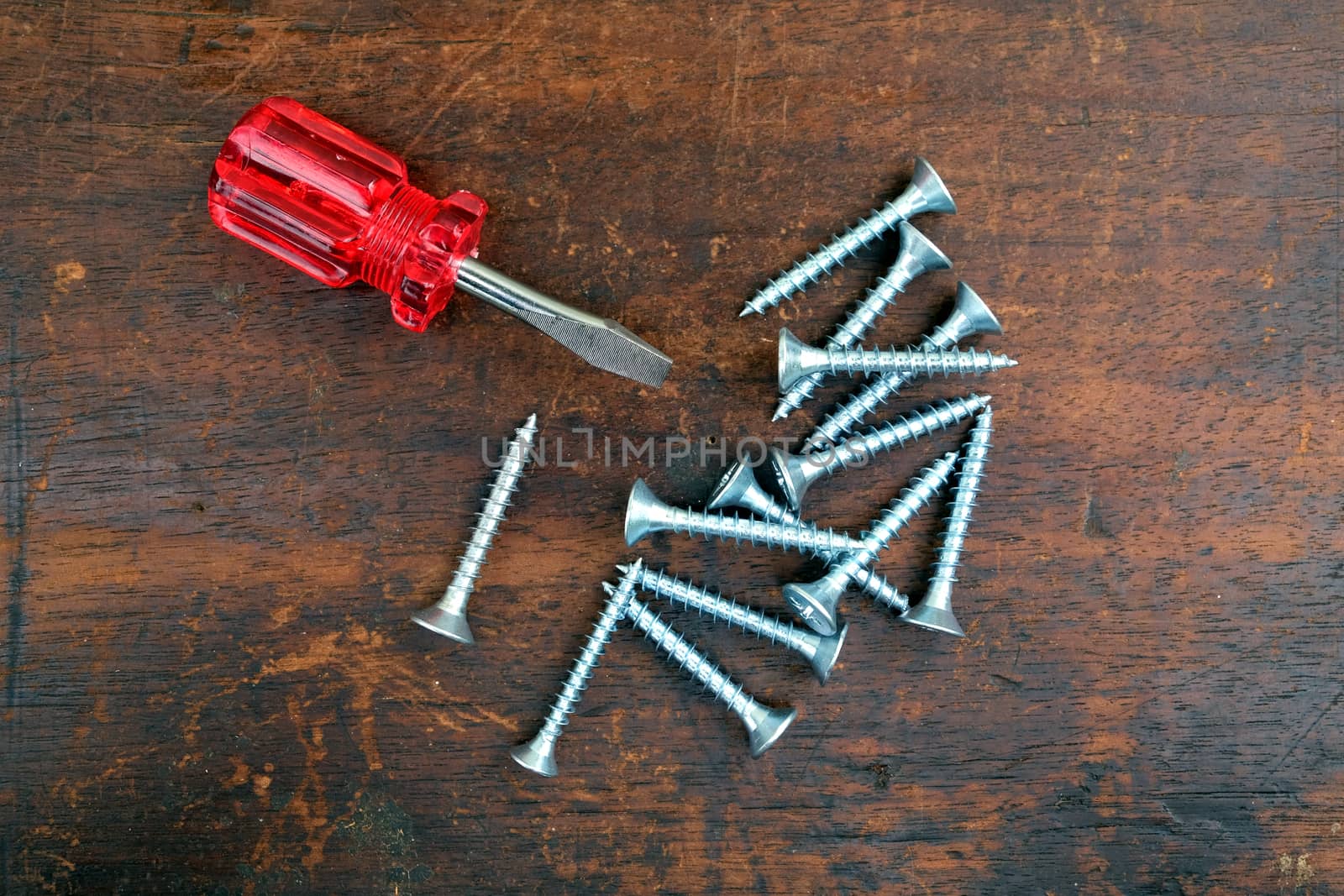 Some many silver screws and small handy screw driver on brown wooden surface top view closeup view