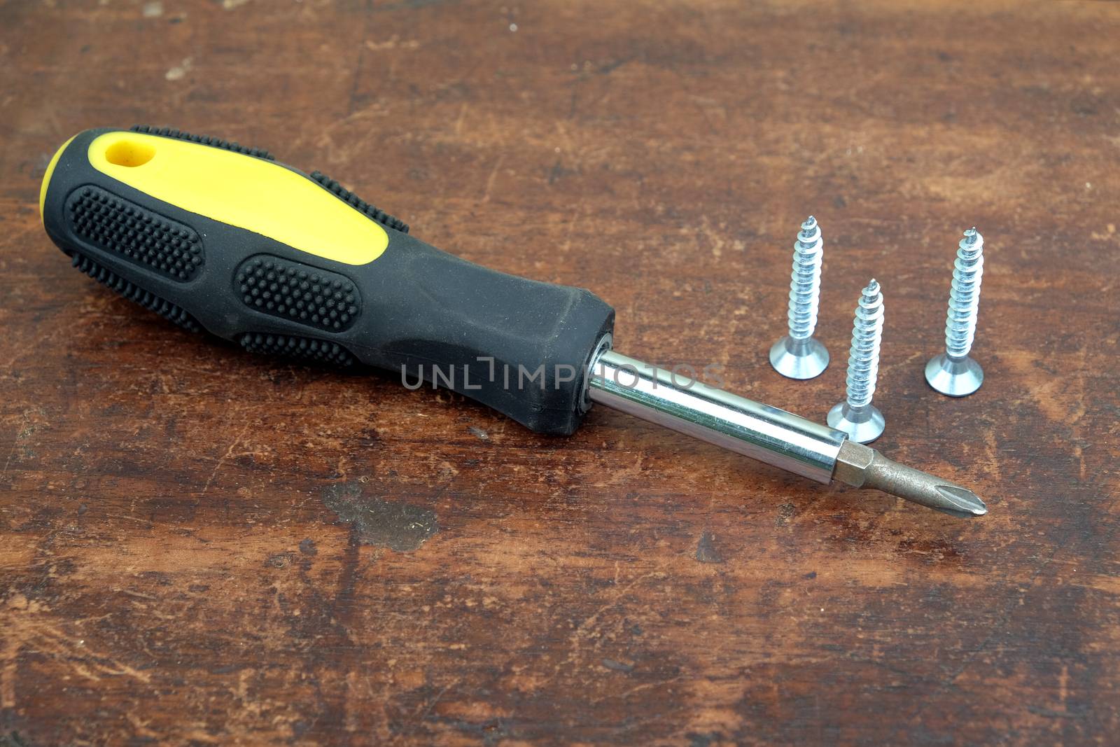 Handy screw driver and three sharp screws on brown wooden background by dymaxfoto