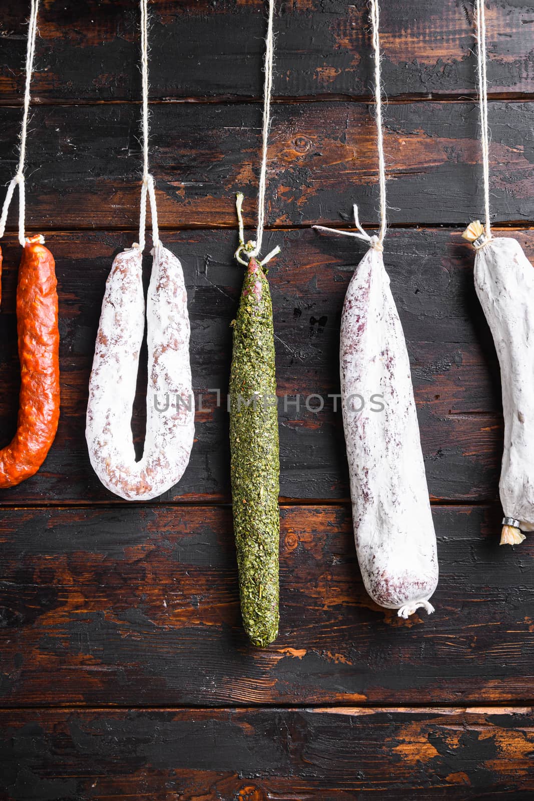 Spanish dry sausages hang from a rack at market on wooden surface.