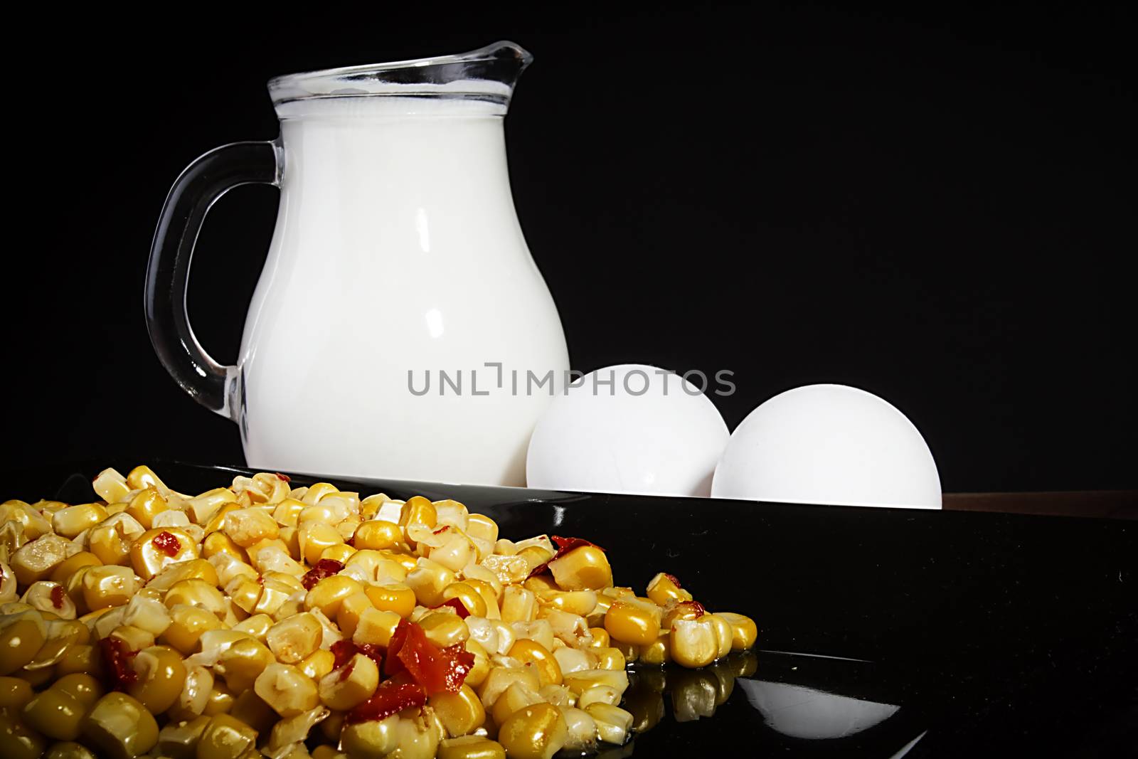 Corn and milk in a jug on a black reflective surface