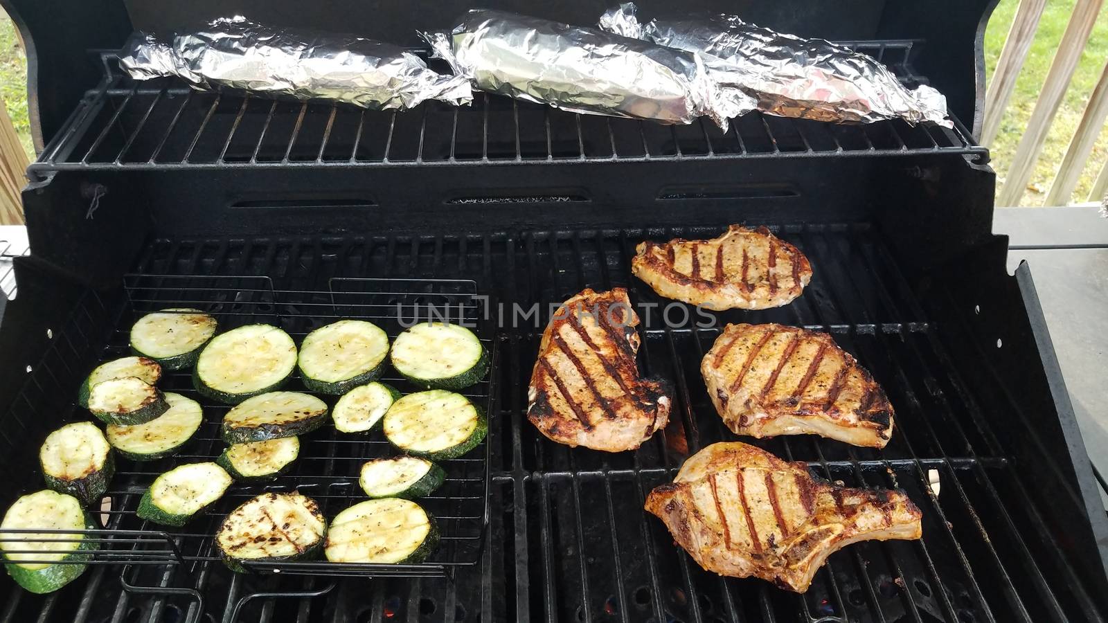 zucchini and pork chops cooking on barbecue grill with corn