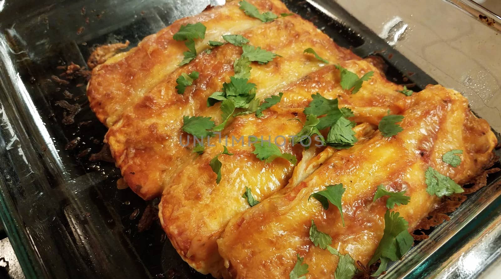 cheesy enchiladas with cilantro in glass container on stove by stockphotofan1