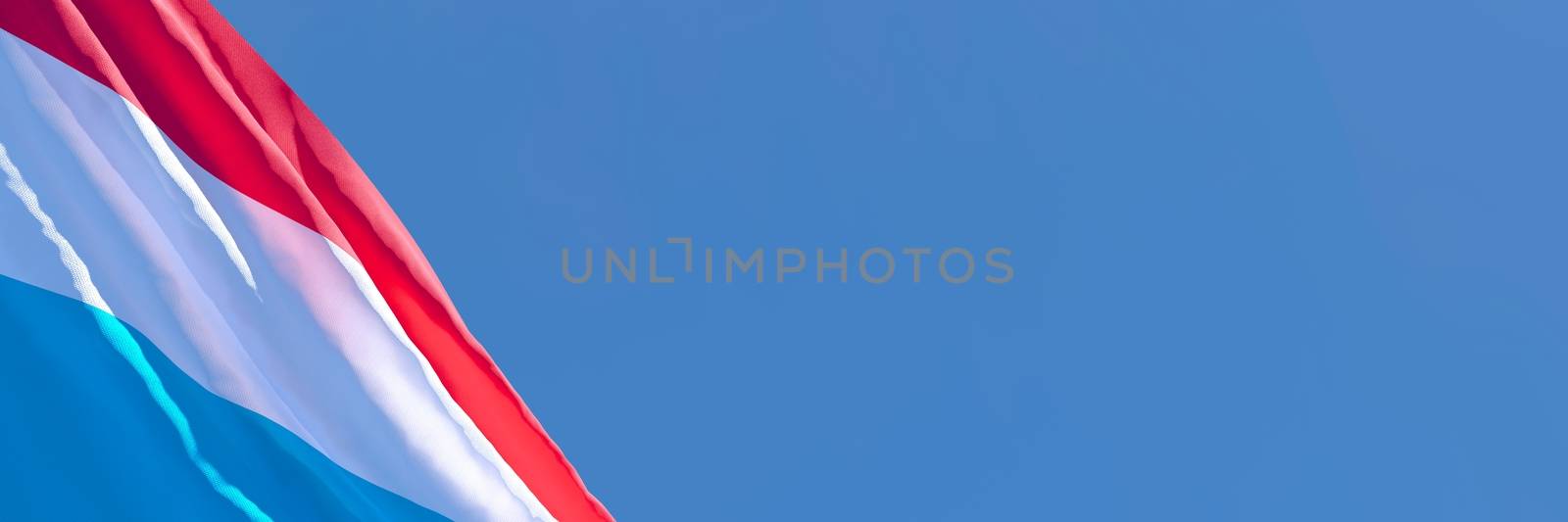 3D rendering of the national flag of Luxembourg waving in the wind against a blue sky