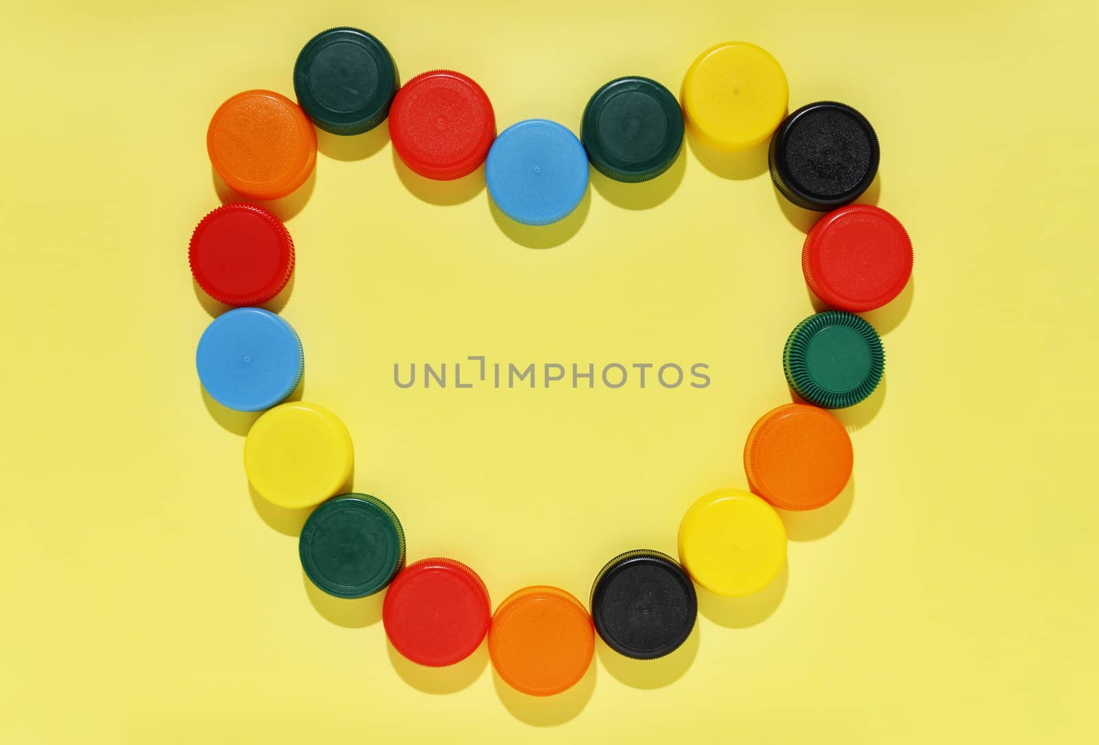 Multicolored plastic bottle caps forming heart shape on yellow background