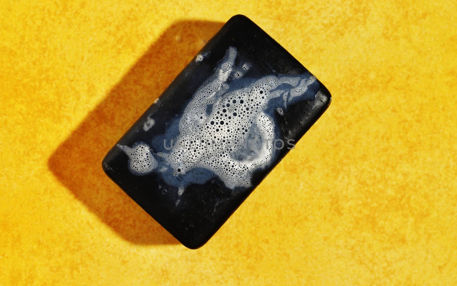 Wet bar of black soap with bubbles on yellow bright background