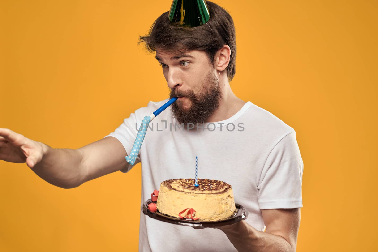 Handsome man with a beard and in a cap celebrating a birthday party yellow background. High quality photo