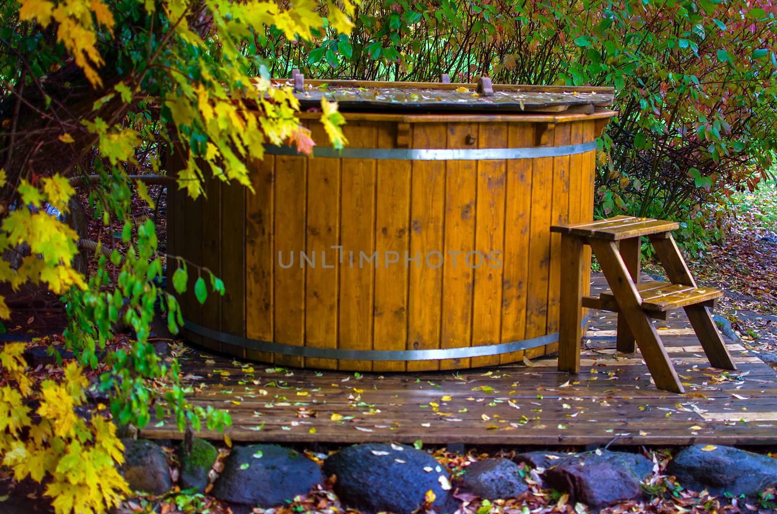 Old western style wooden bathtub in barrel shape. Wooden bath basin filled with water on autumn background