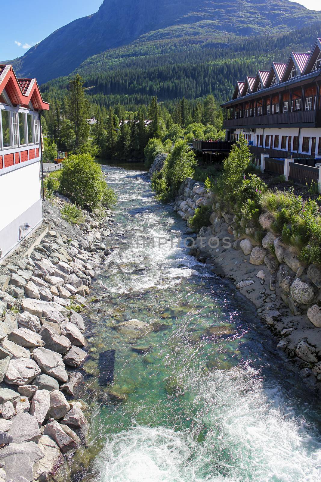 Flowing beautiful turquoise river water between houses in Hemsedal, Norway. by Arkadij