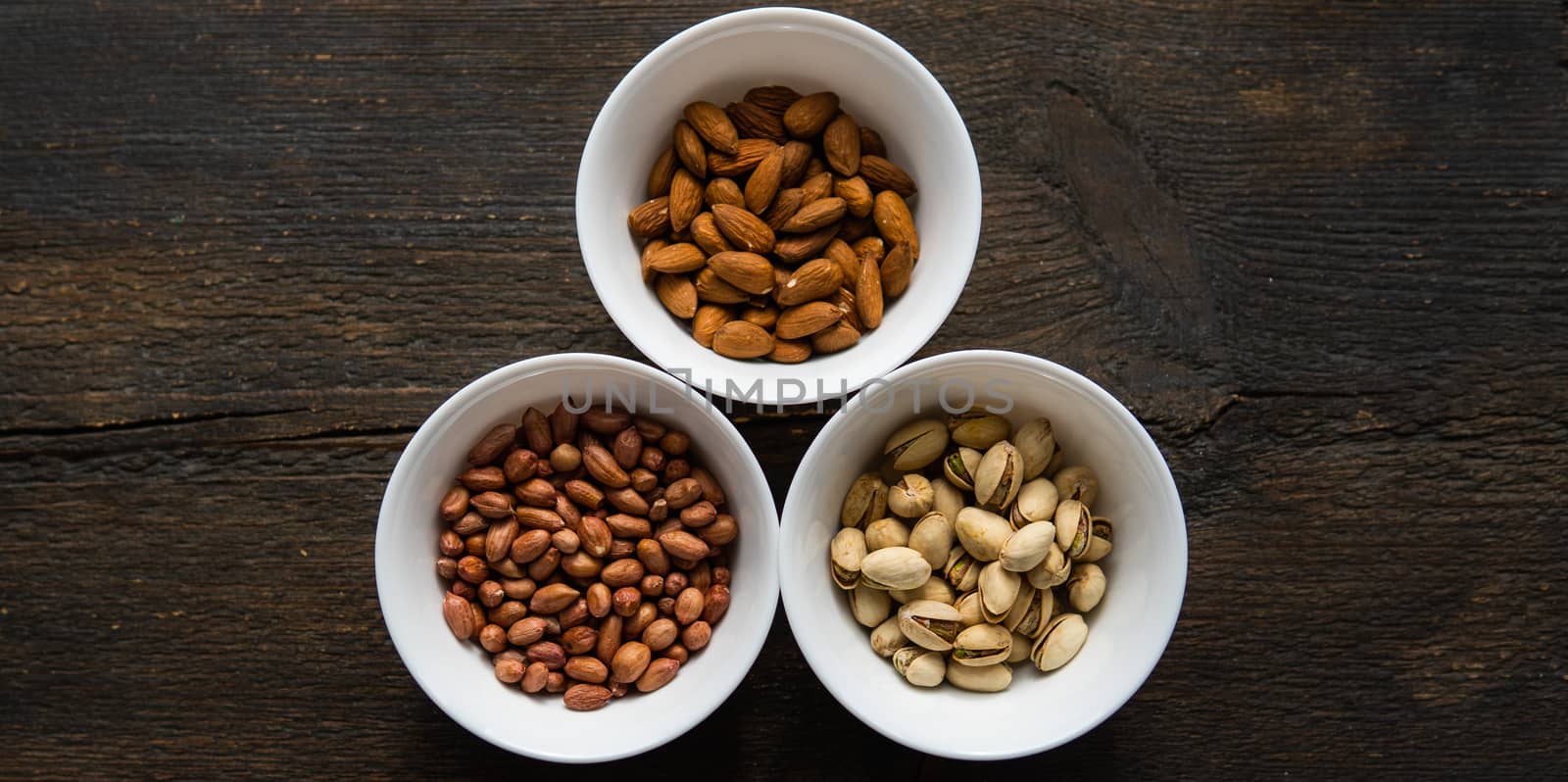 Pistachio, peanut and almond in a small plates which standing on a black table. Nuts is a healthy vegetarian protein and nutritious food