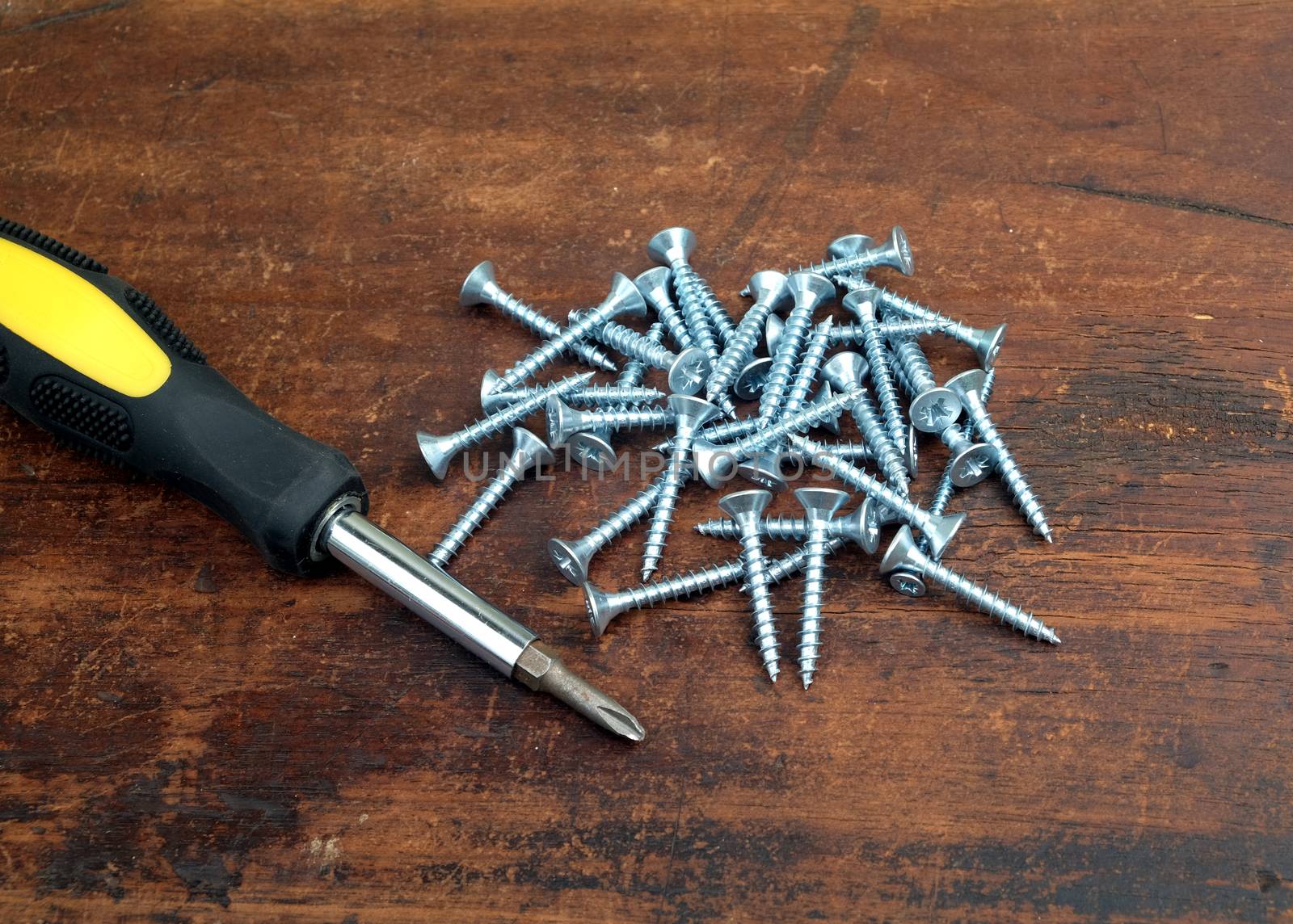 Many light gray screws and old screw driver on brown wooden background closeup view
