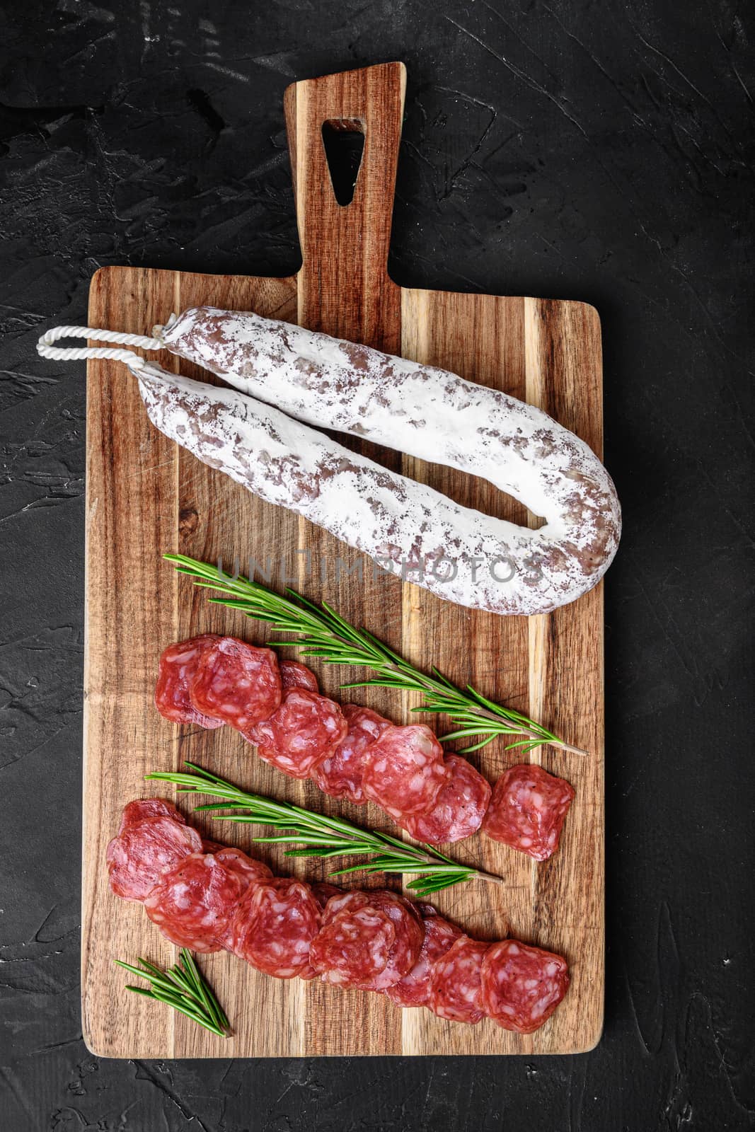 Fuet salami wurst cut in slices and whole sausage on black background, top view.