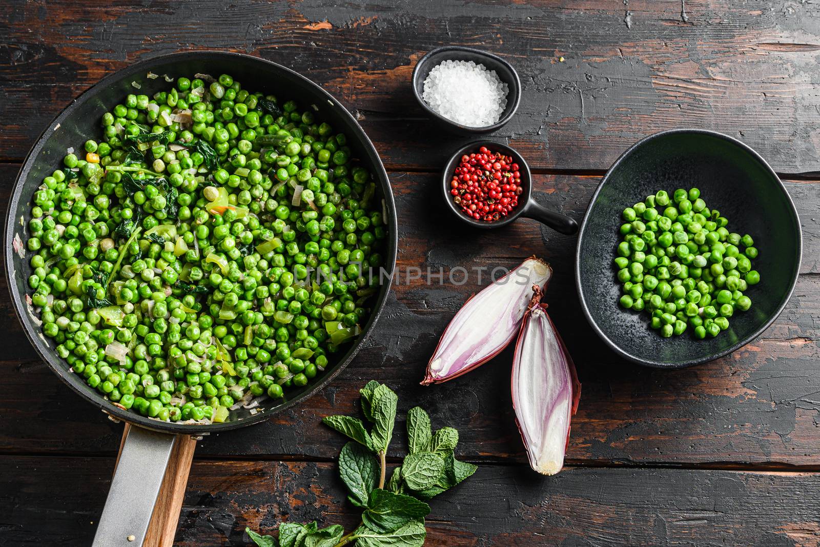 Traditional English Mushy Peas ingredients for fish and chips in frying pan and peas in bowl with mint shallot pepper and salt top view over old pub wood table.