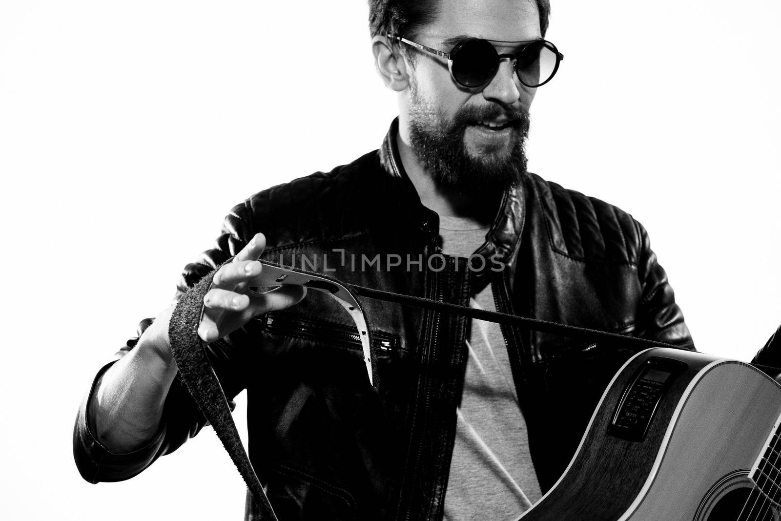 A man plays the guitar in a black leather jacket with sunglasses on a light background by SHOTPRIME