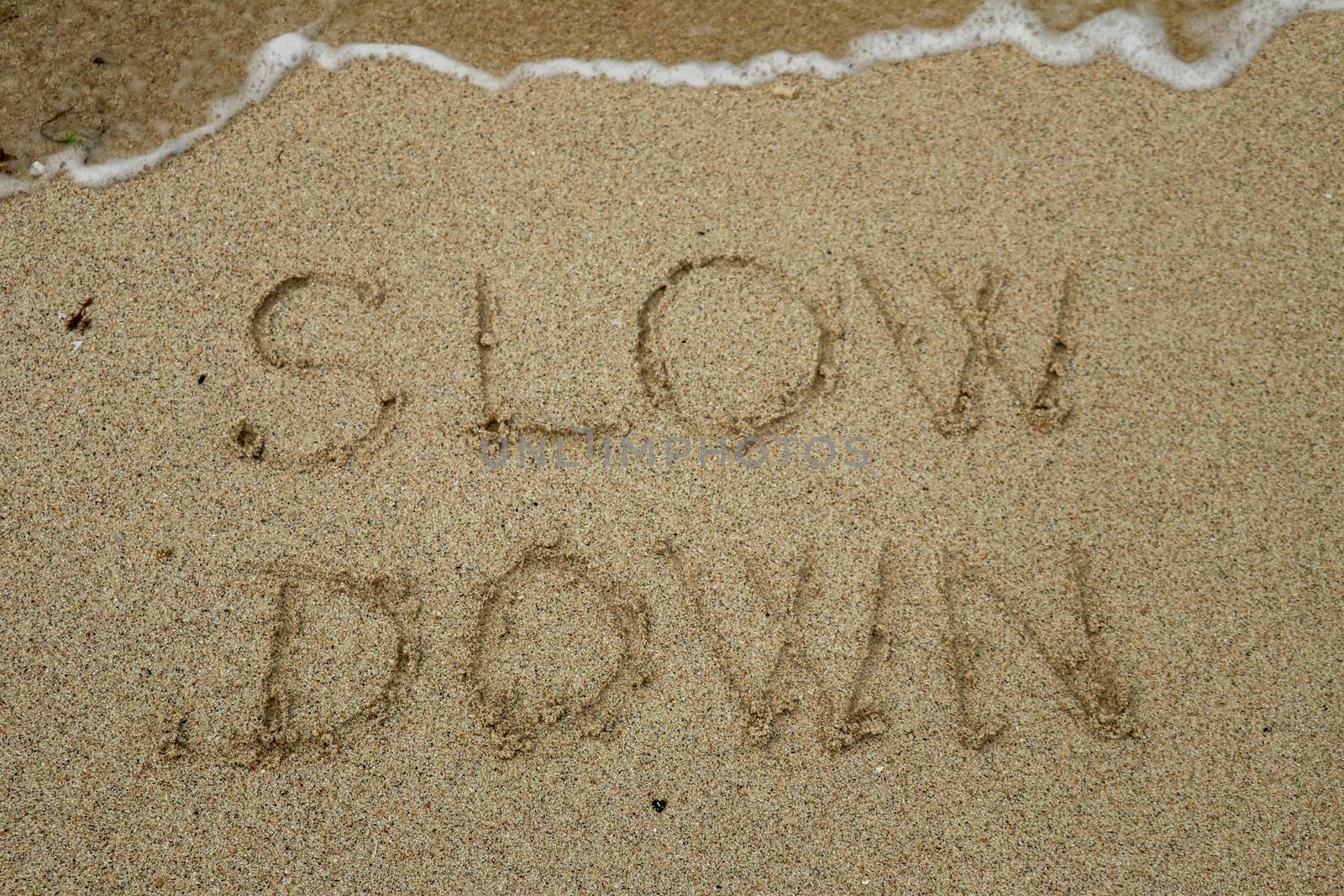 slow down, mindfulness concept written on sand.
