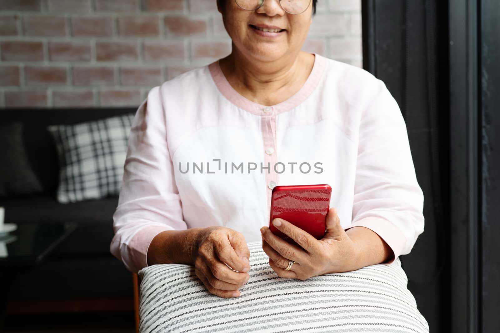 smiling senior woman using mobile phone while sitting on sofa at home