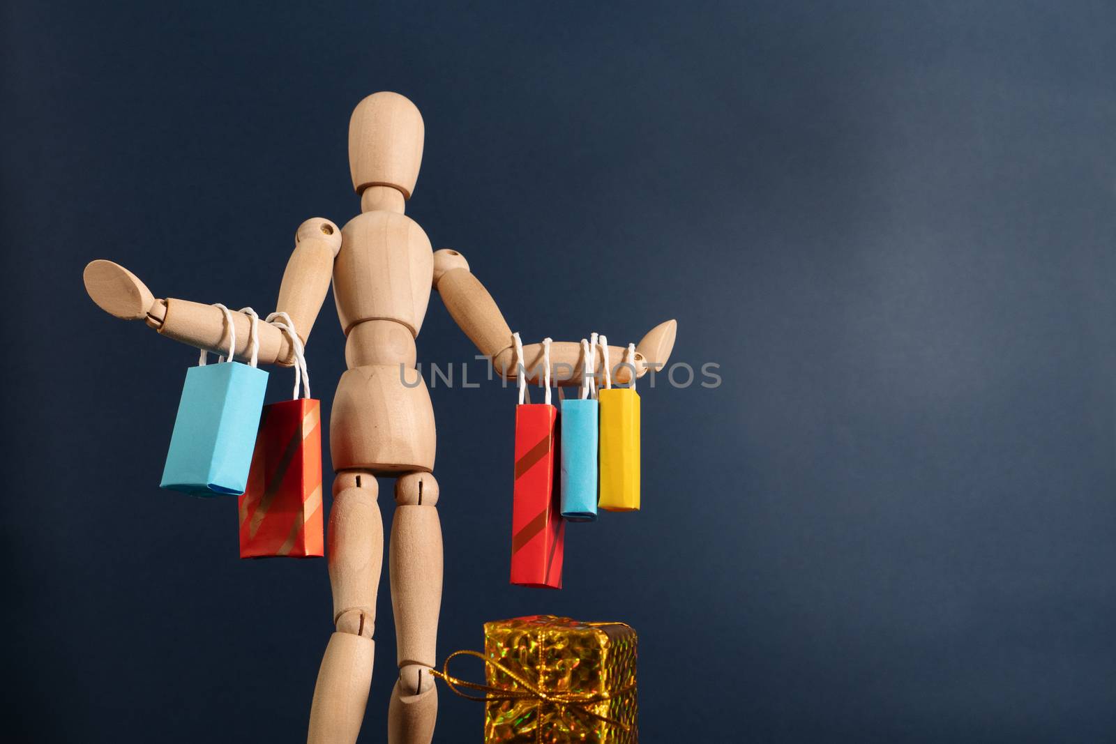 Cheerful happy shopaholic wooden doll with lots of shopping bags on arm
