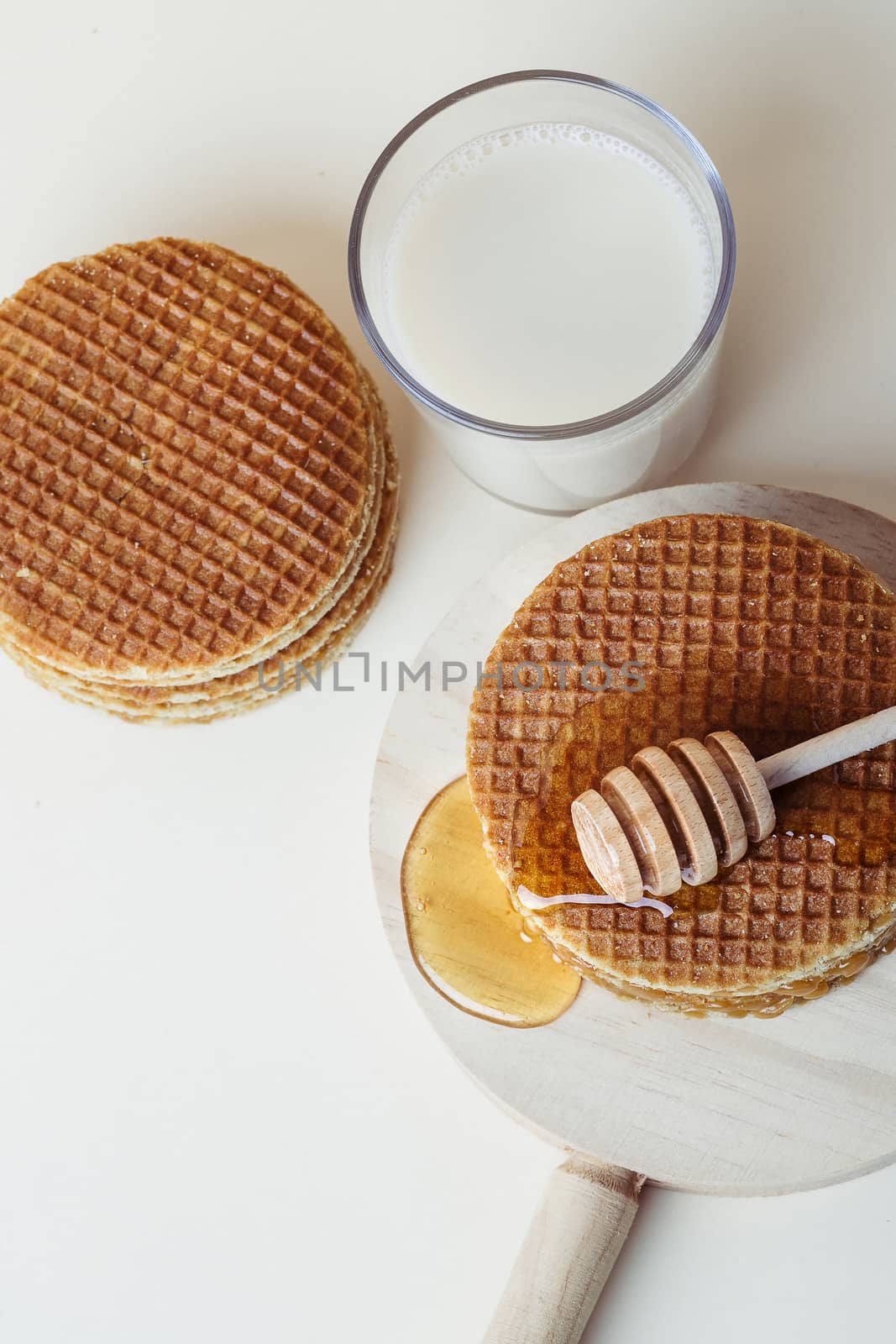 Honey dipper pouring honey over a pile of waffles on a wooden tray. Top view.