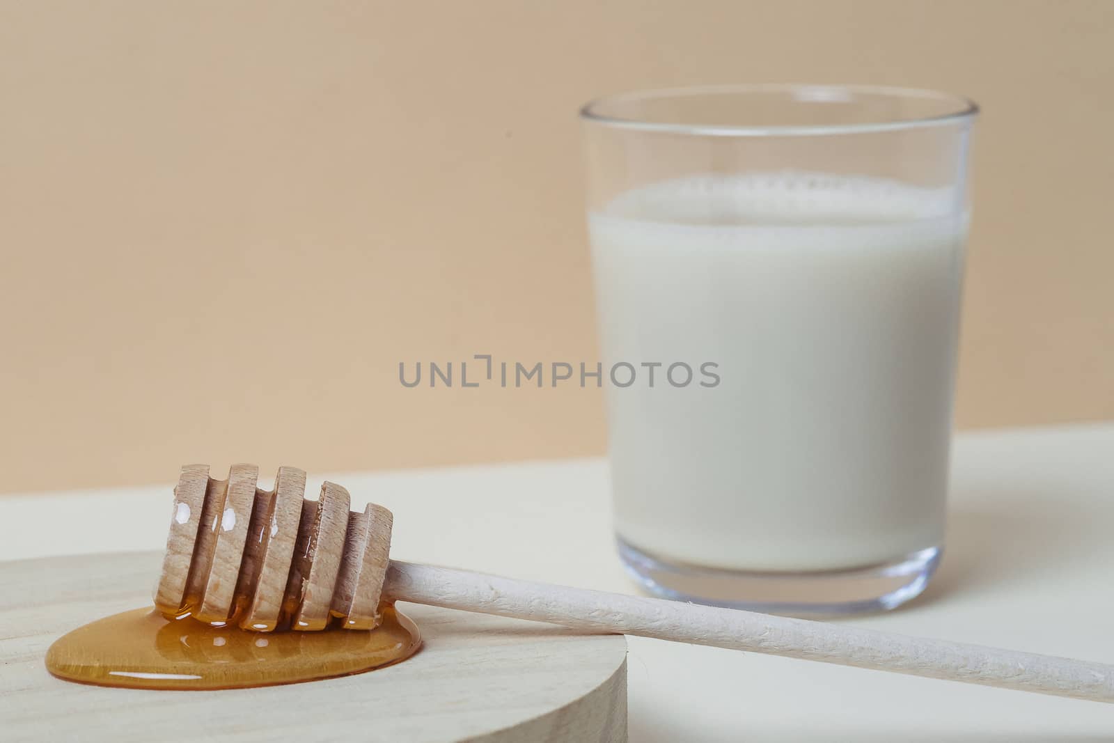 A honey dipper on a wooden tray and a glass full of milk. Copy space.