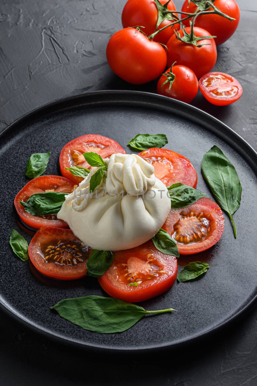 Burrata, Italian fresh cheese made from cream and milk of buffalo or cow. on black plate over black stone surface top view close up by Ilianesolenyi