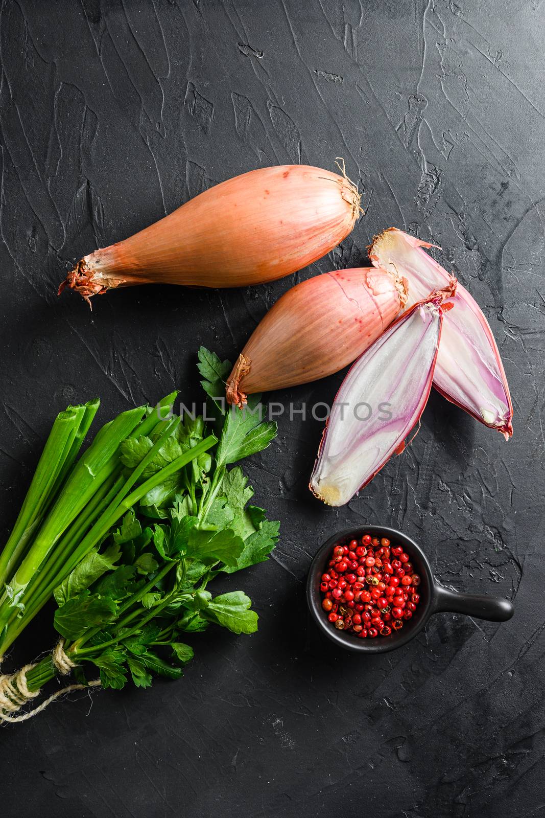 Shallot, eschalot or scallion raw ripe onions with greens and rose peppercorns sliced and halved black concrete textured background top view vertical by Ilianesolenyi