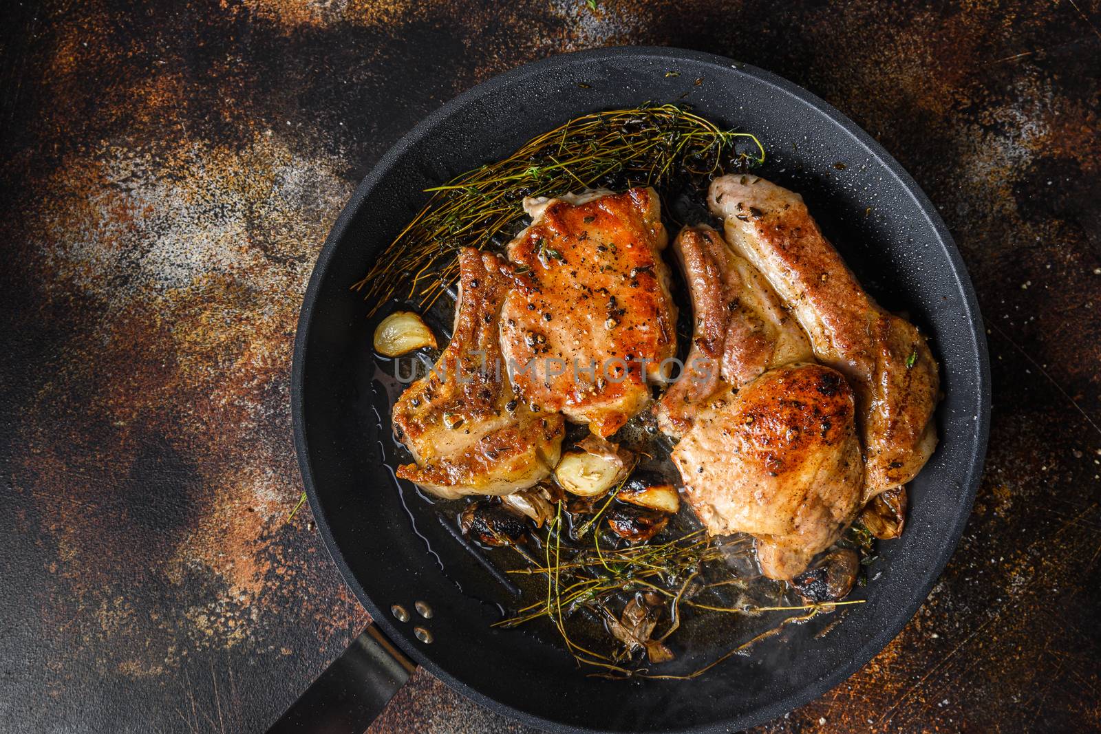 Grilled organic pork cutlets with herbs on bone in grill frying pan hot with smoke and hot oil just from fire, top view cooking bone with seasonings rustic metal background close up