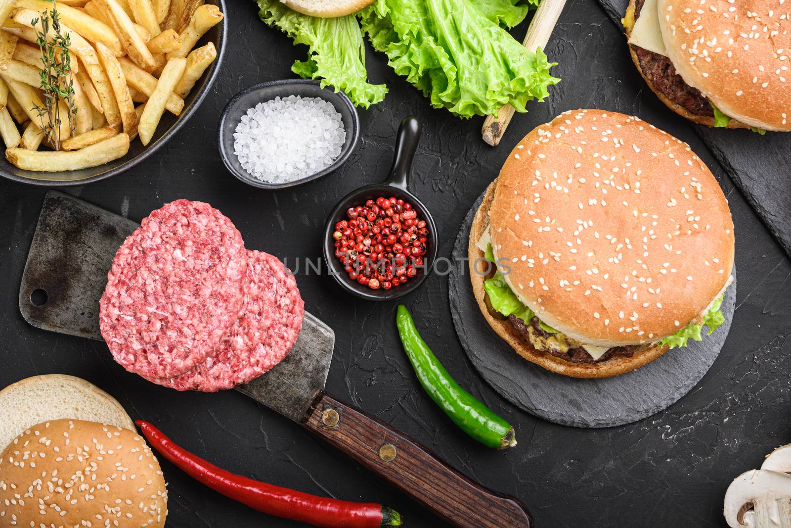 Homemade beef burgers with ground beef cutlets on black textured background.
