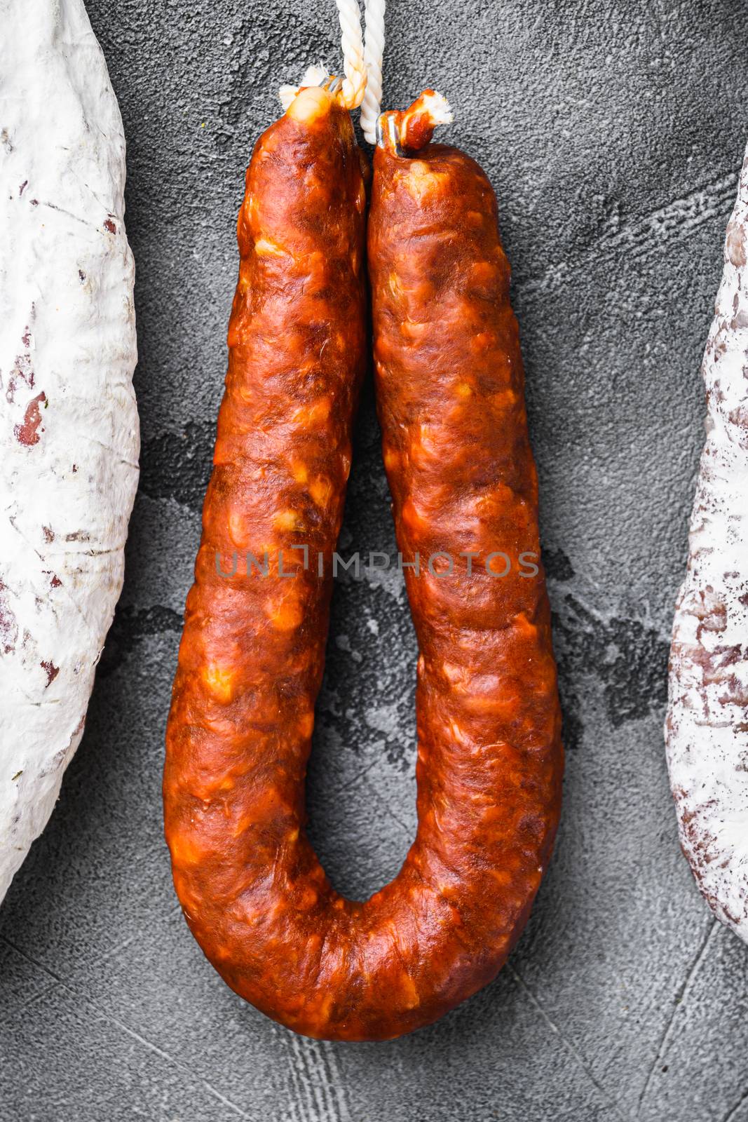 Spanish dry salami from a rack at market on grey textured background.