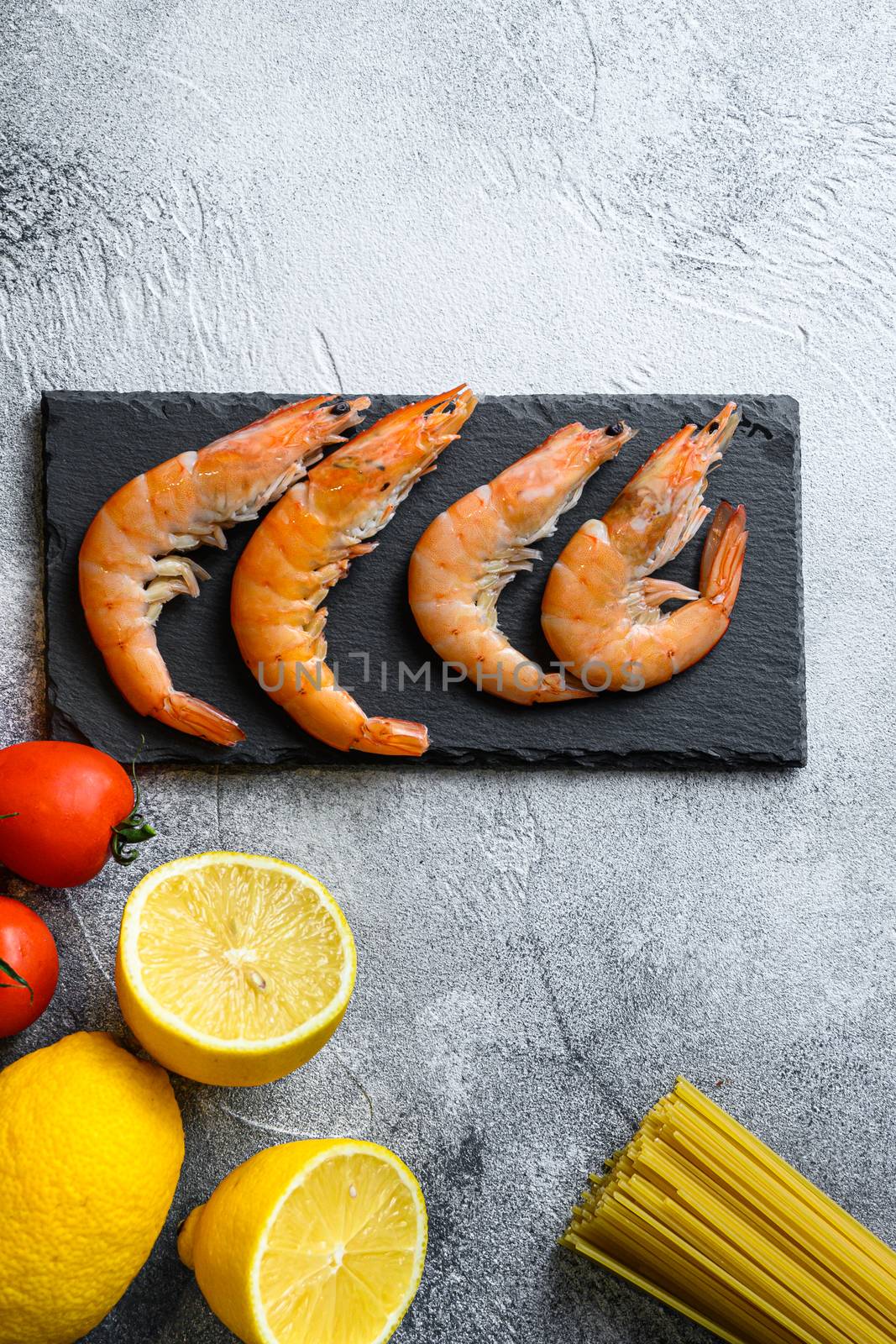 Lemon Garlic Shrimp on black stone slate with Spaghetti Ingredients On grey slate stone table with , tomatoes, lemon, ,mint classic recipe top view space for text.