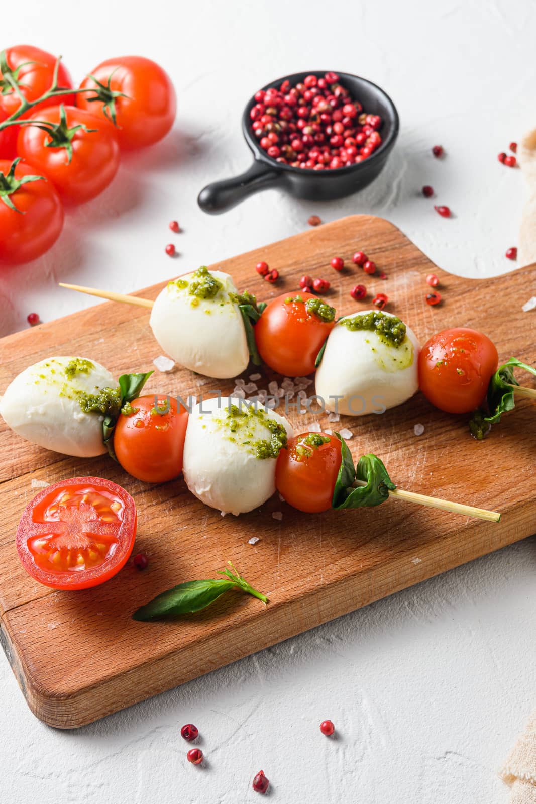 talian food - caprese salad - skewer with tomato, mozzarella and basil, pesto sauce, mediterranean diet concept on old chopping board and linen cloth top view vertical selective focus with ingredients by Ilianesolenyi