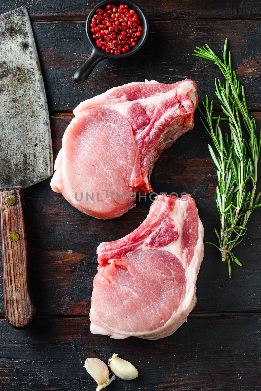 Organic bio Pork steaks, fillets for grilling, baking or frying, Fith butcher cleaver ower dark wood planks. Overhead view by Ilianesolenyi