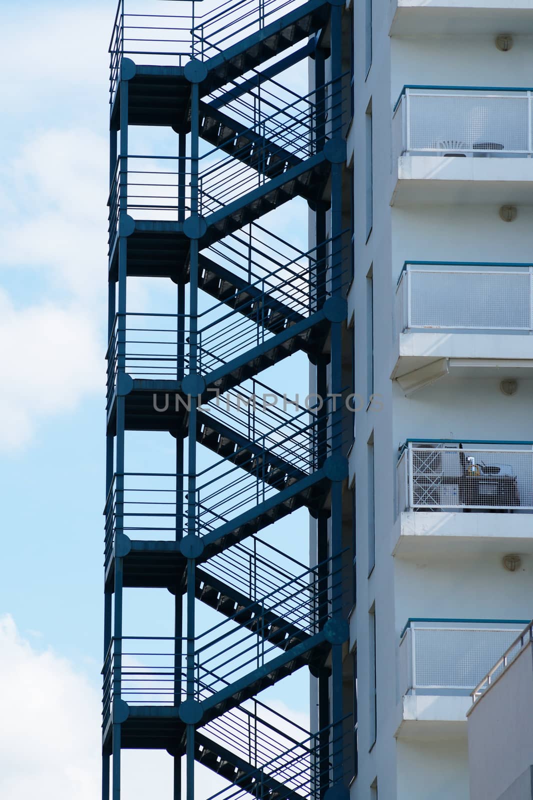 metal fire escape on the wall of a residential building against the background of the sky by Annado