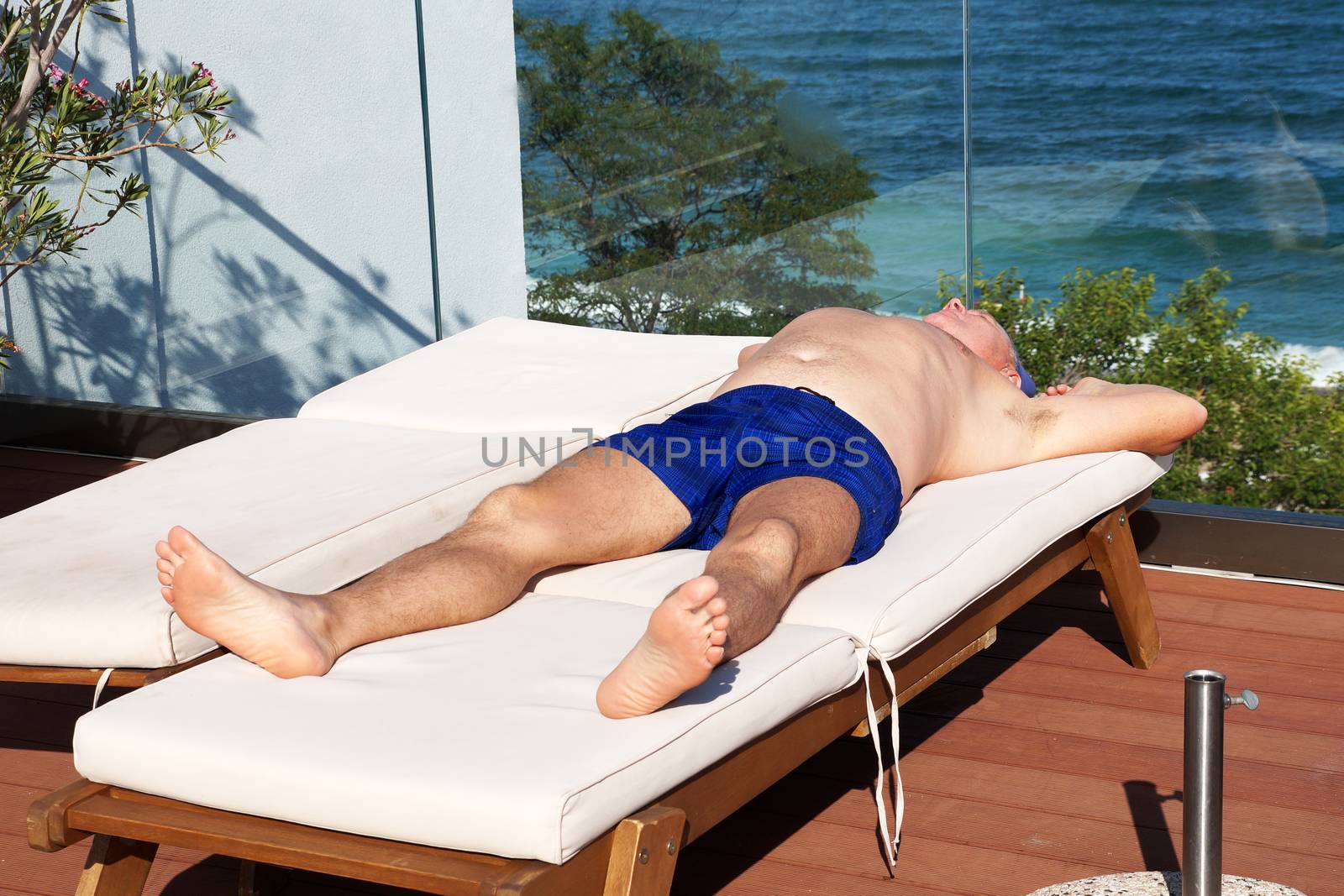 a man sunbathes on a sun lounger on a sun terrace overlooking the sea by Annado