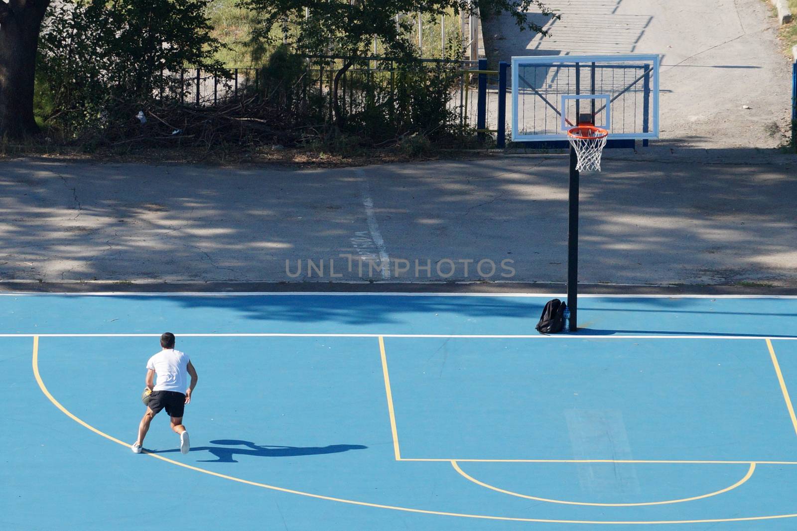 young man training with a ball on an outdoor basketball court by Annado