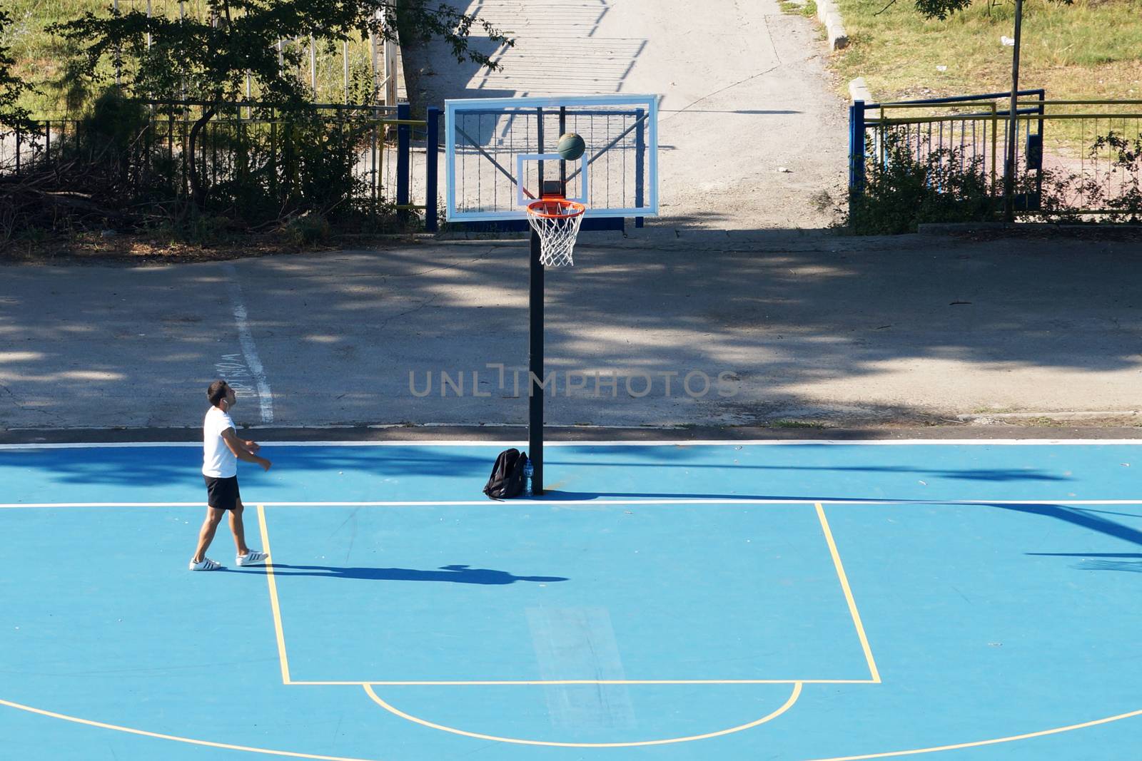 young man training with a ball on an outdoor basketball court by Annado