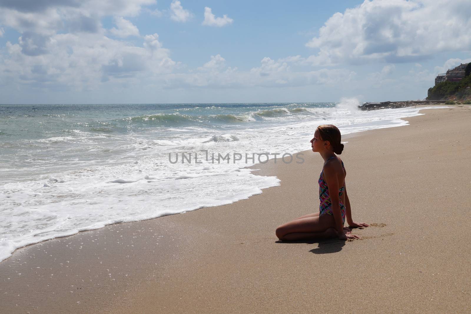 teenage girl sitting alone on the wet sand and looking at the sea.