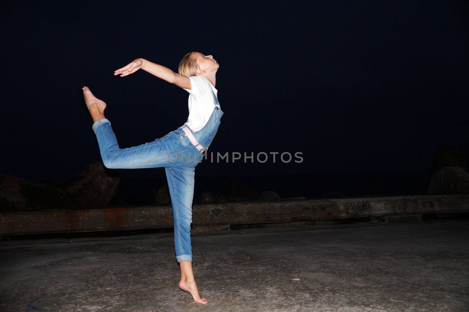 barefoot teenage girl dancing ballet on an empty pier at night by Annado