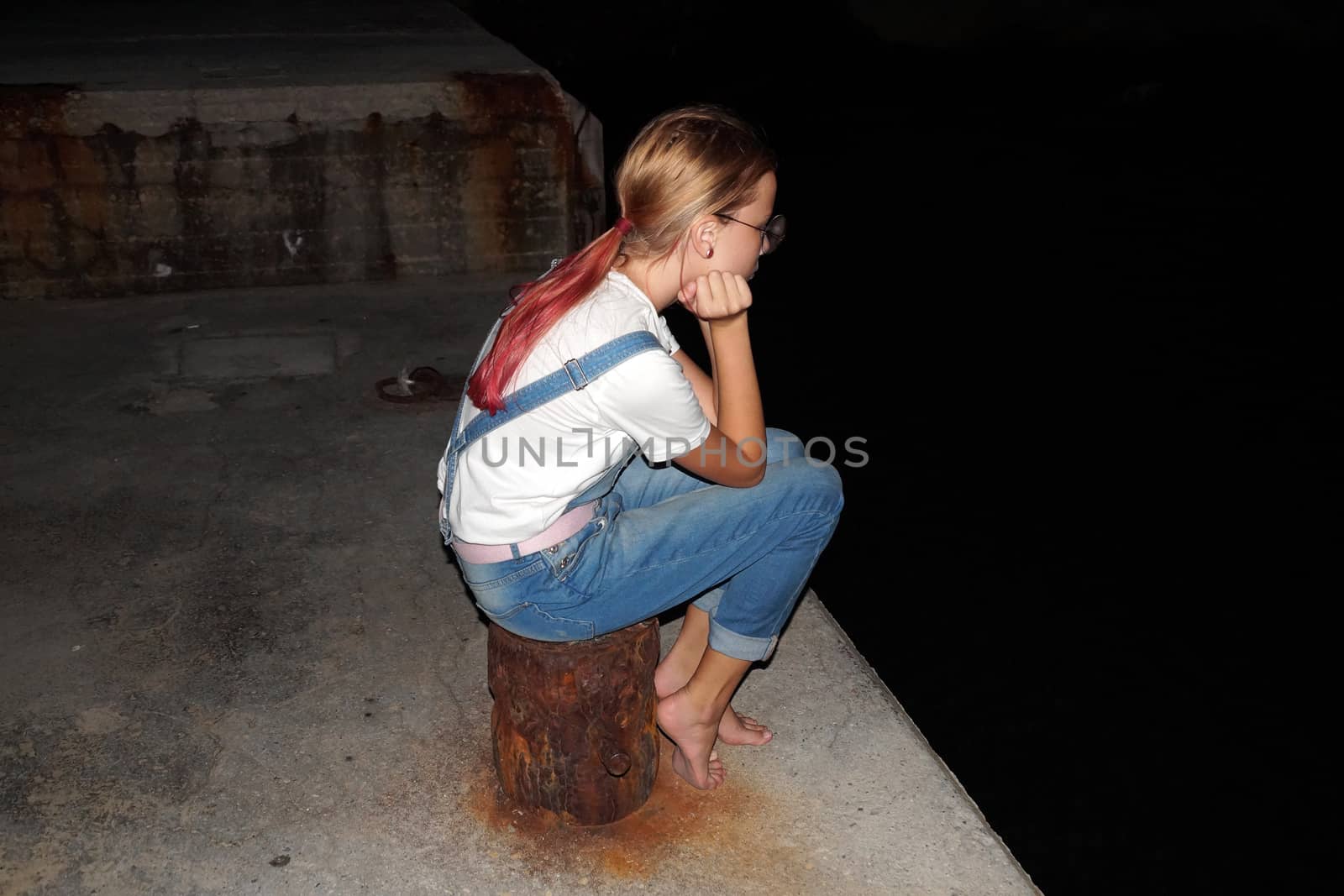 sad teenage girl sitting alone on the pier at night by Annado