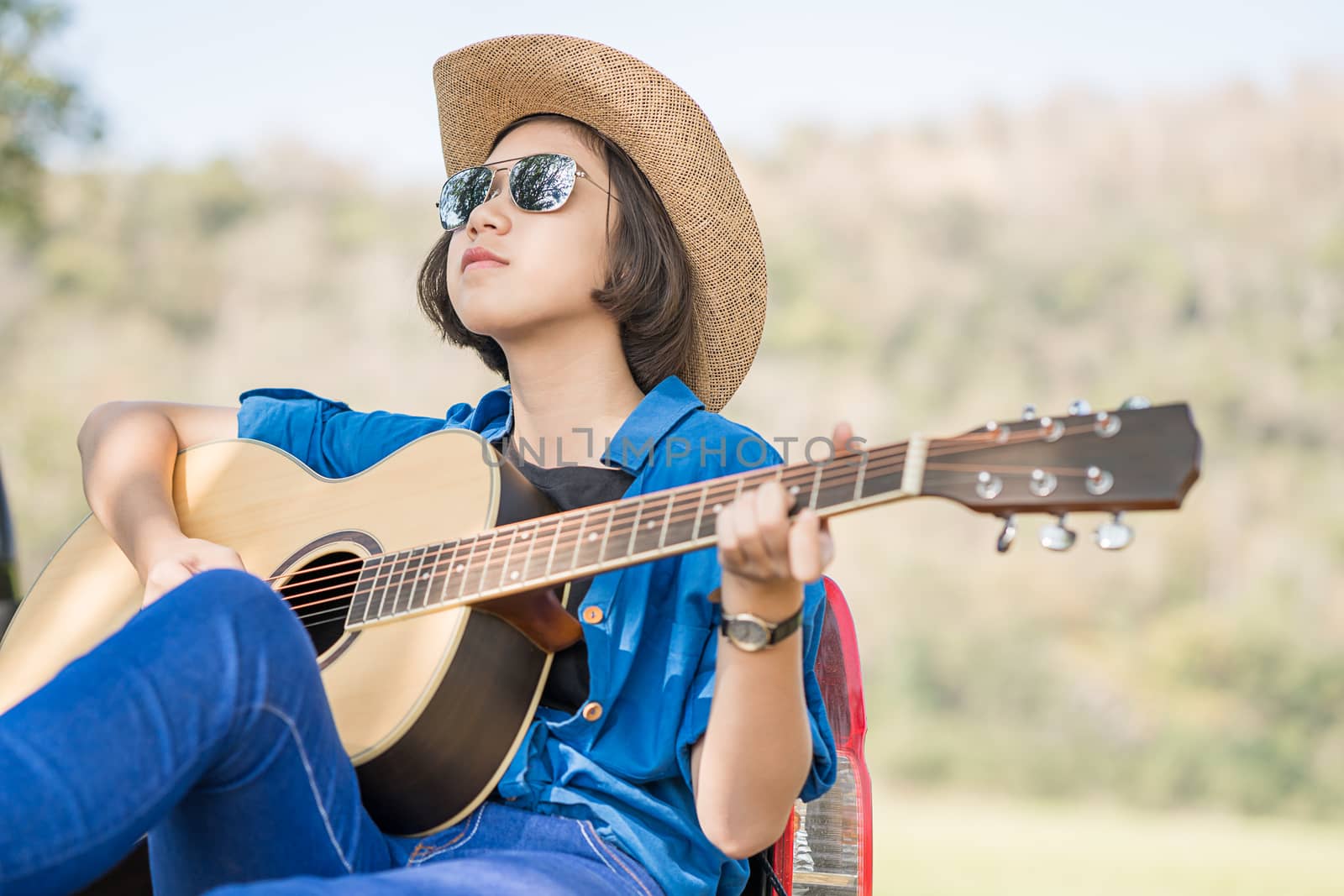 Close up young asian women short hair wear hat and sunglasses playing guitar in countryside Thailand