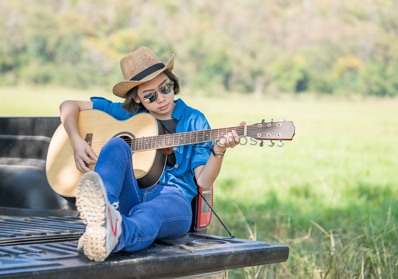 Woman wear hat and playing guitar on pickup truck by stoonn