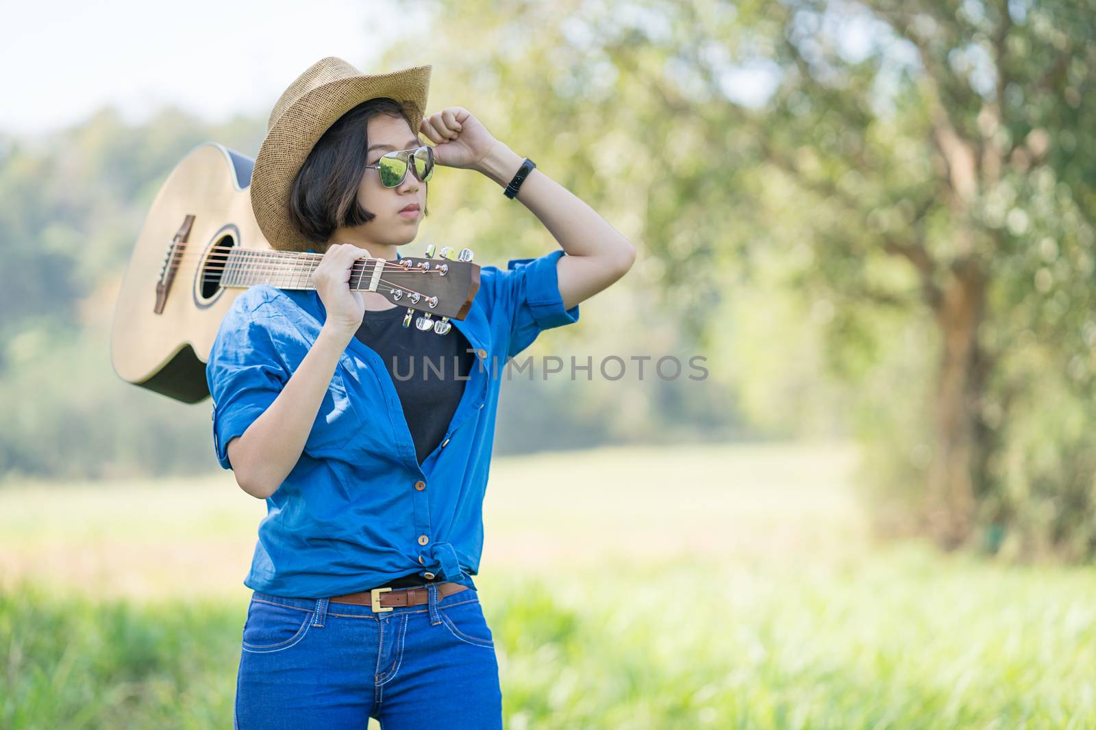 Woman wear hat and carry her guitar in grass field  by stoonn