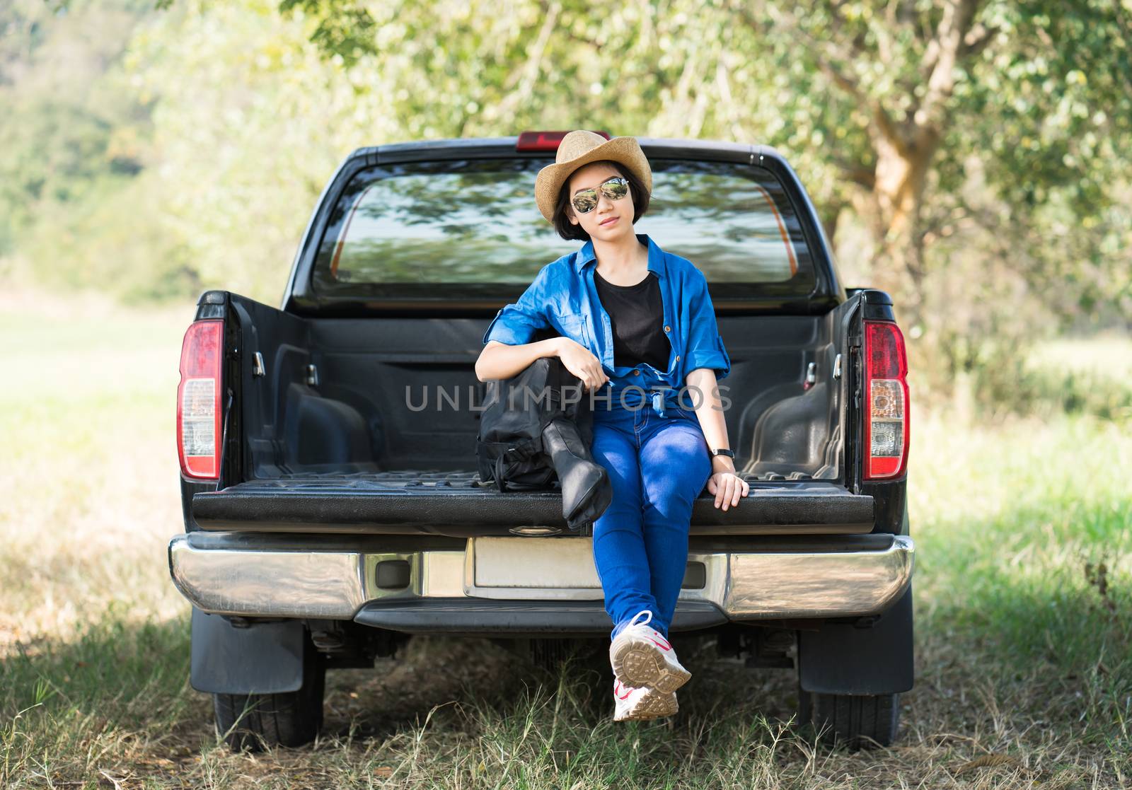 Young asian women short hair wear hat and sunglasses carry her guitar bag ,sit on pickup truck in countryside Thailand