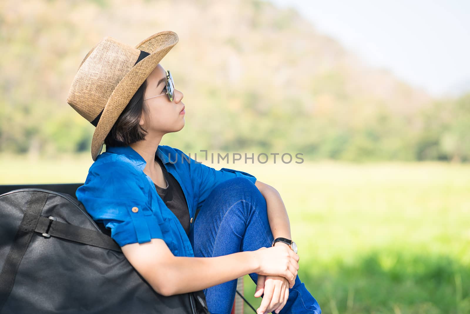 Young asian women short hair wear hat and sunglasses carry her guitar bag ,sit on pickup truck in countryside Thailand