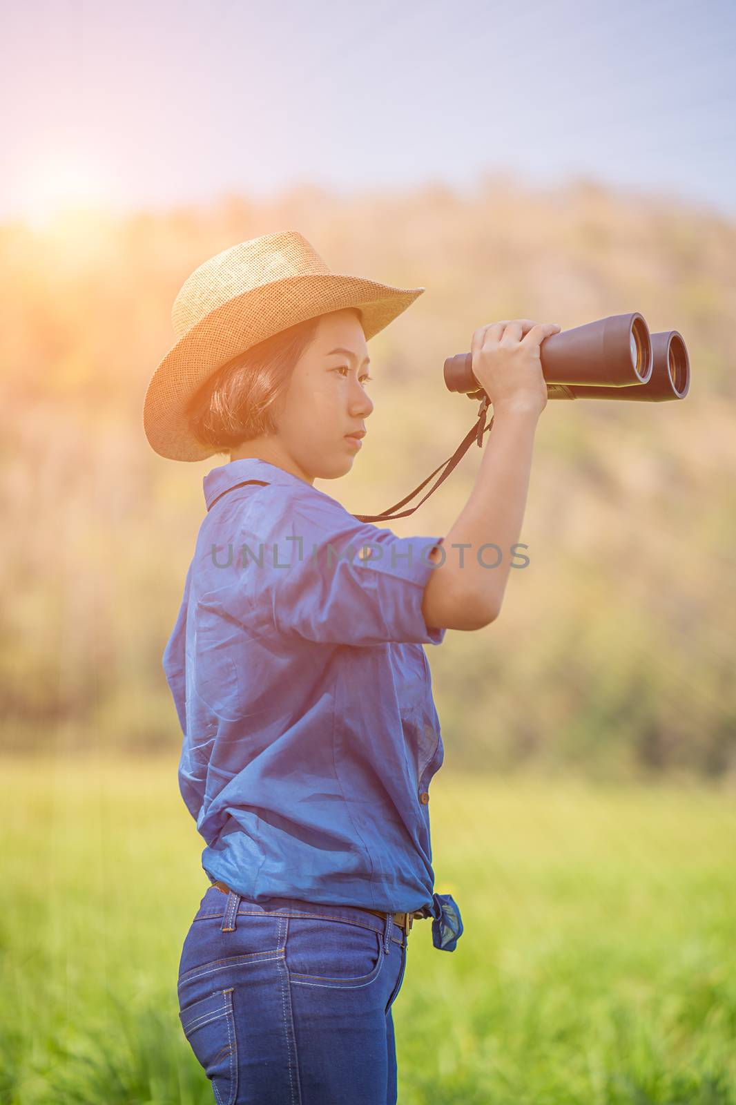 Young asian woman short hair wear hat and hold binocular in grass field countryside Thailand